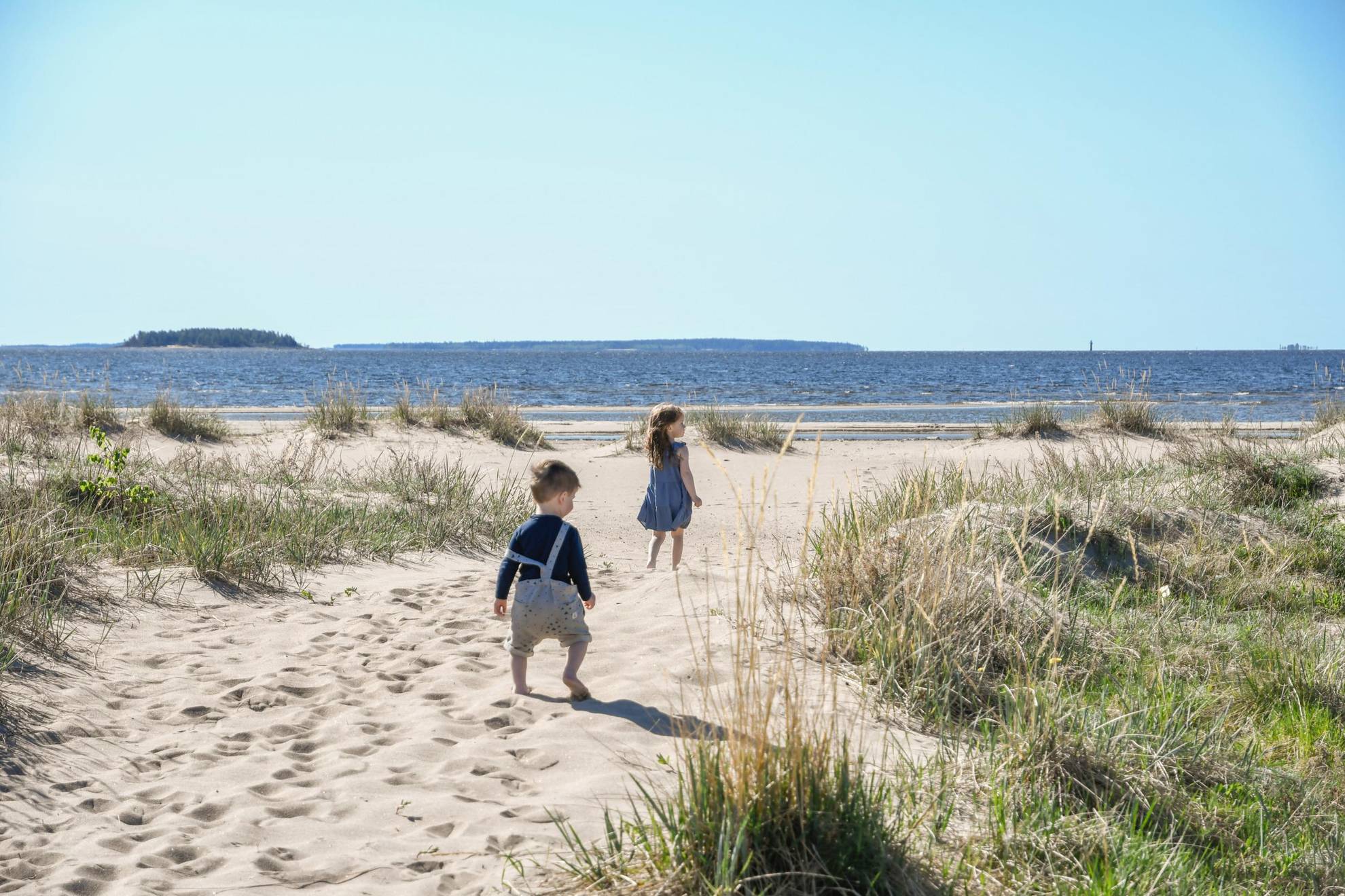 Two children walk on a beach during summer.