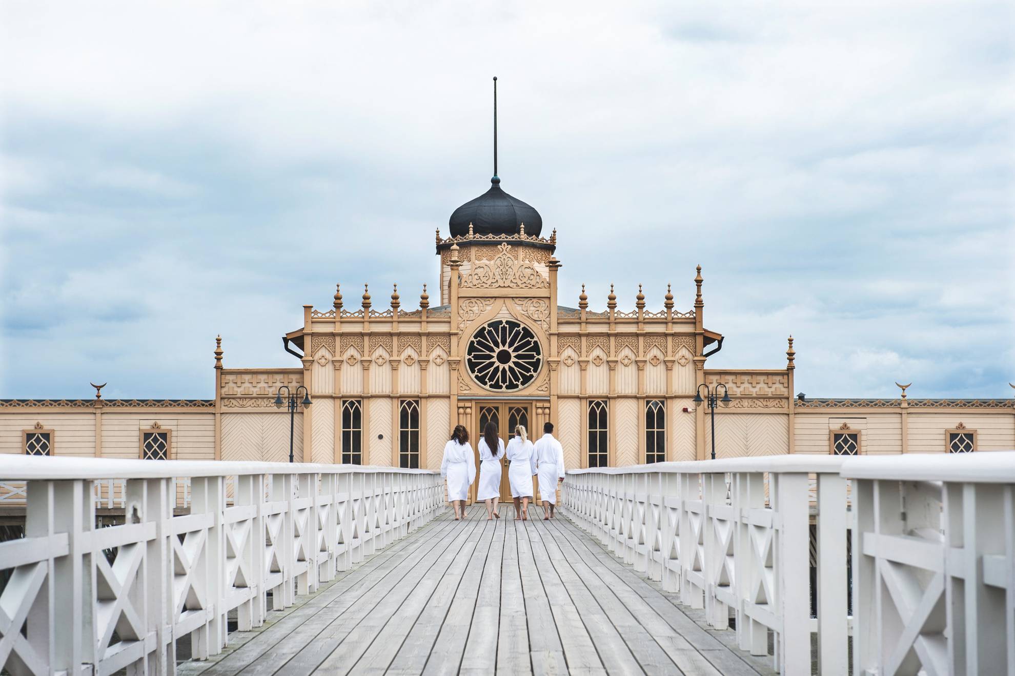 Four persons dressed in bathrobes walking down a jetty to a cold bath house.