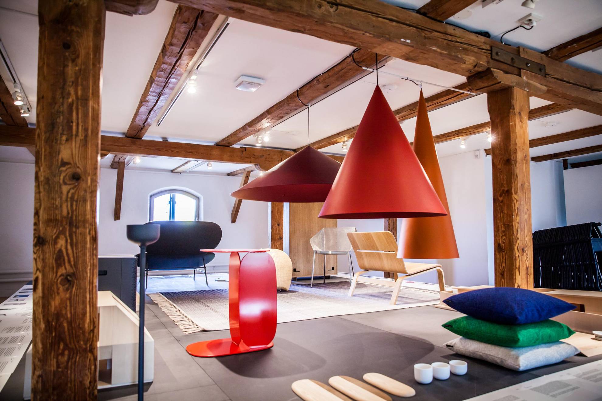 An attic room with wooden beams. Colourful design objects in the room, such as lamps, chairs and pillows.