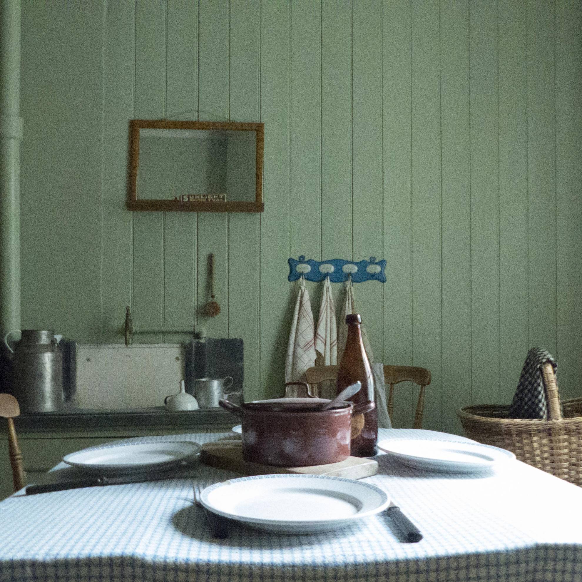 Inside a worker home in the first suburb of Gothenburg during the 19th and 20th centuries. A set table with a iron pot in the middle. On a green wooden wall hang a mirror.
