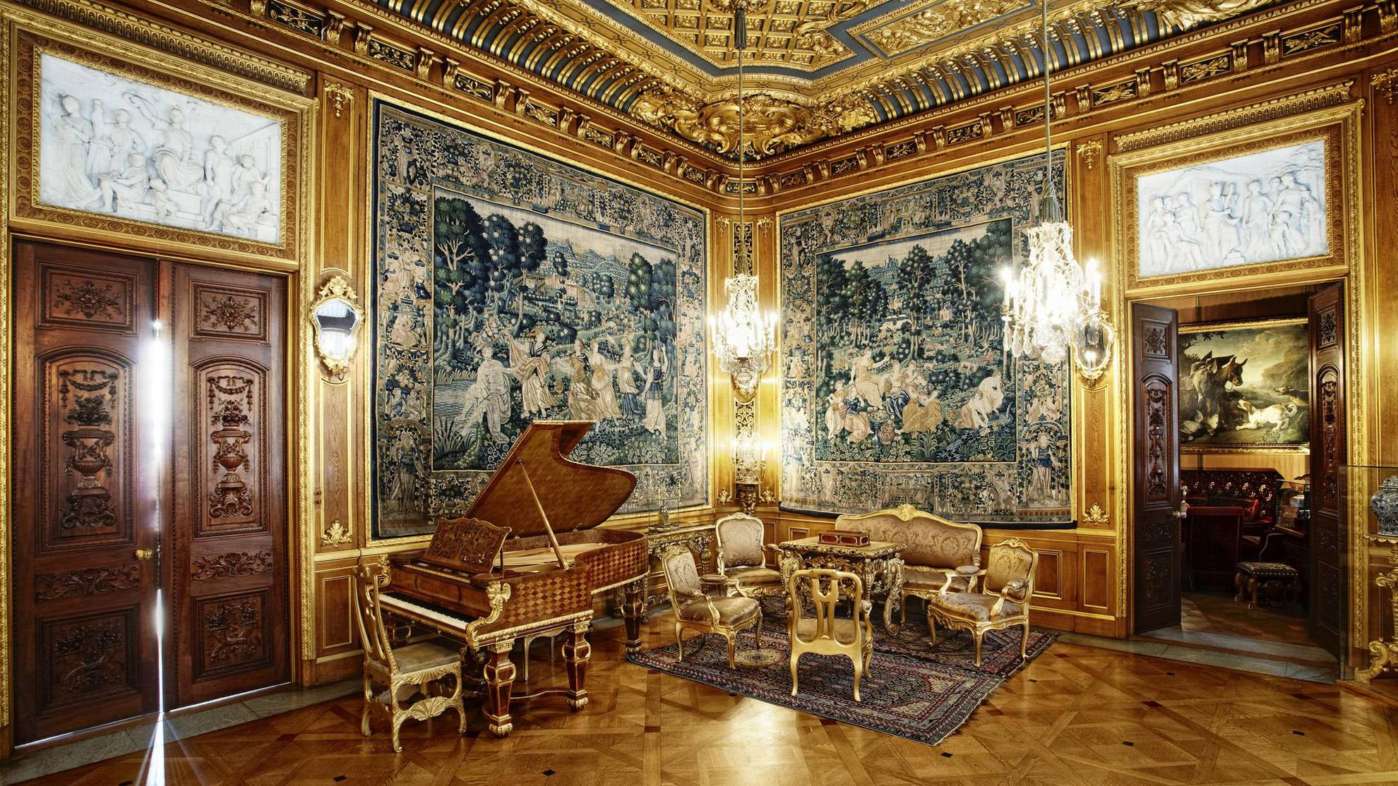 The luxurious, golden sitting room of Hallwyl house, with large paintings, a grand piano, golden furniture and chandeliers.