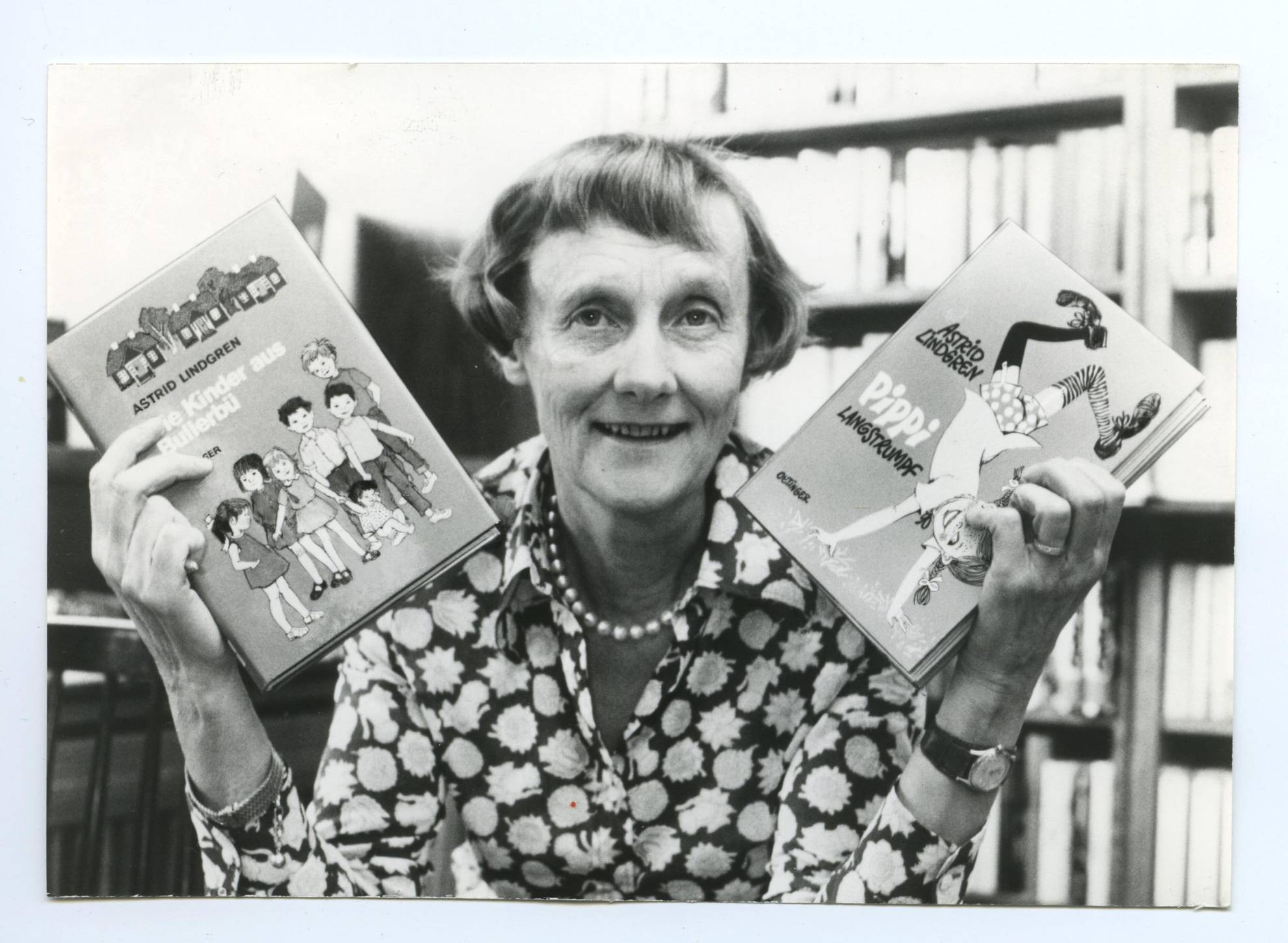 A black and white portrait of the author Astrid Lindgren holding her book Pippi Longstocking in one hand and the book the Noisy Village children in the other hand.