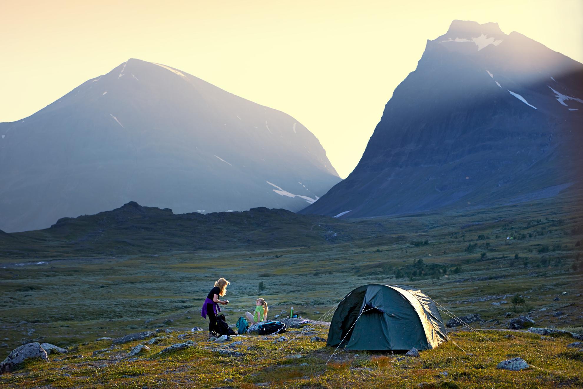 Two girls camping in the wild with mountains in the background.