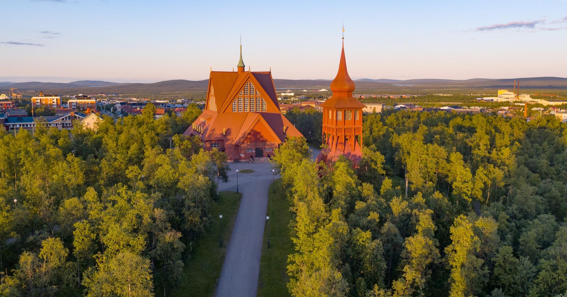 The red building of Kiruna church is surrounded by greenery.