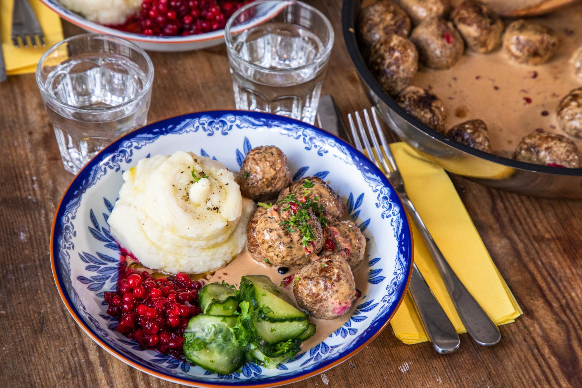 A plate with vegan meatballs, sauce, pickled cucumber, lingonberry jam and mashed potatoes.