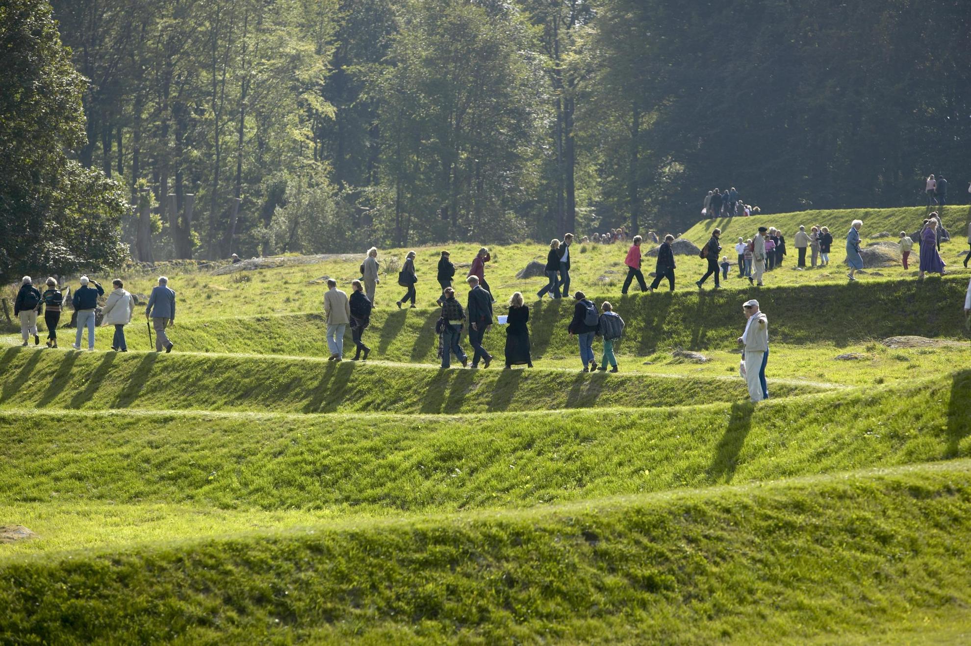 A art work called “Eleven Minute Line” in a sculpture park. Several people are walking on the art work, a 500 meter winding ridge of earth, stone and grass.