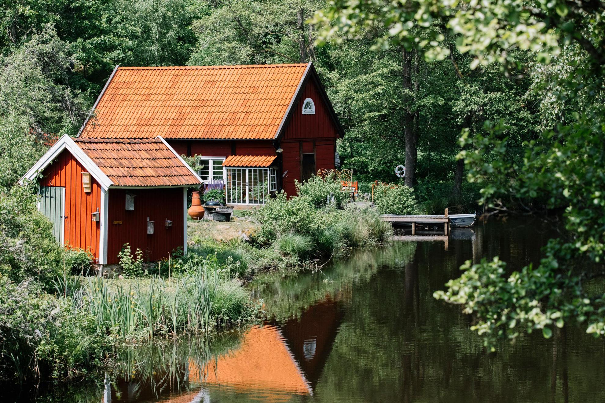 Next to a lake with lush forest around, there's a traditional red cottage and a small red guest house.
