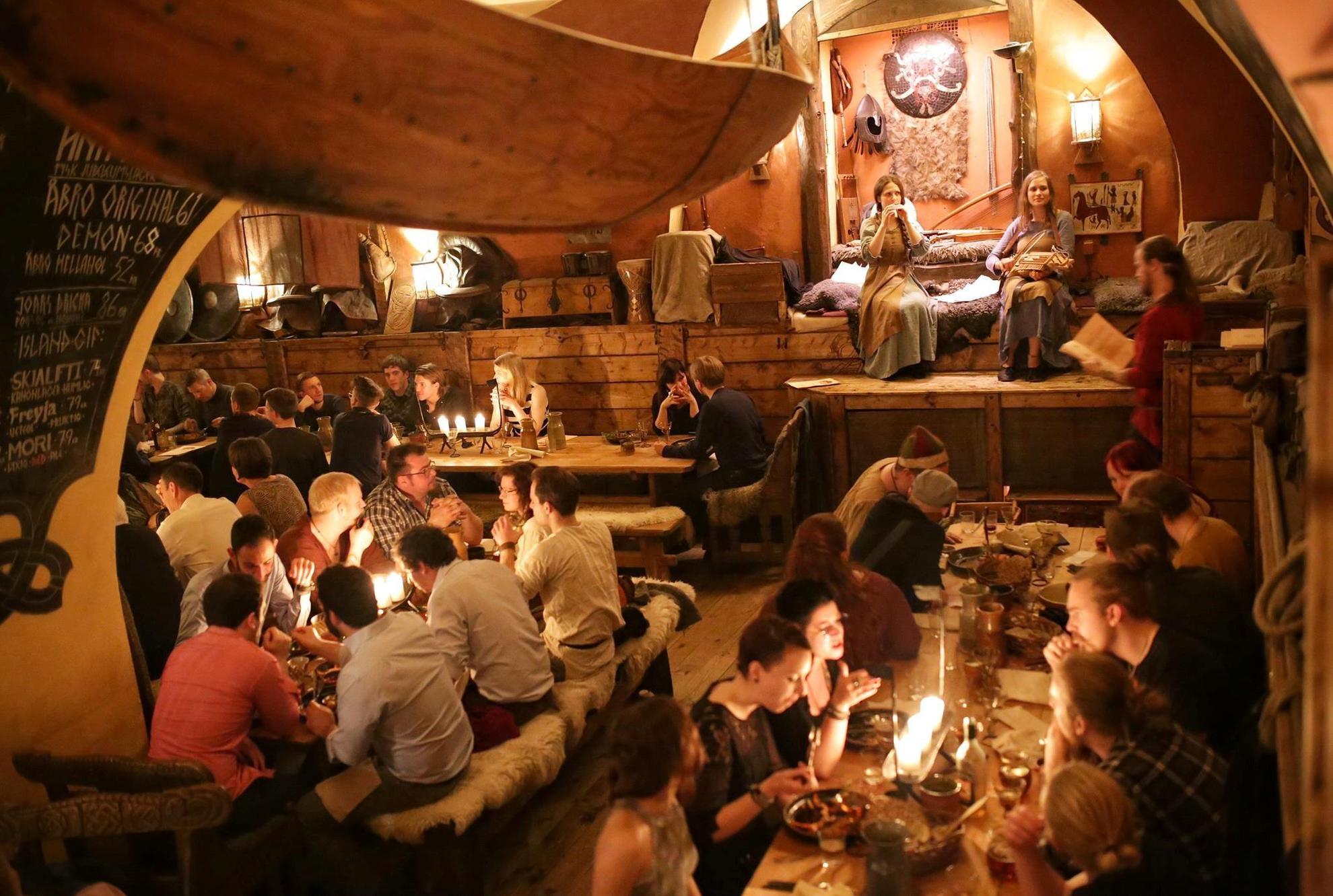 A viking themes restaurant filled with people. On the small stage is two women playing music.