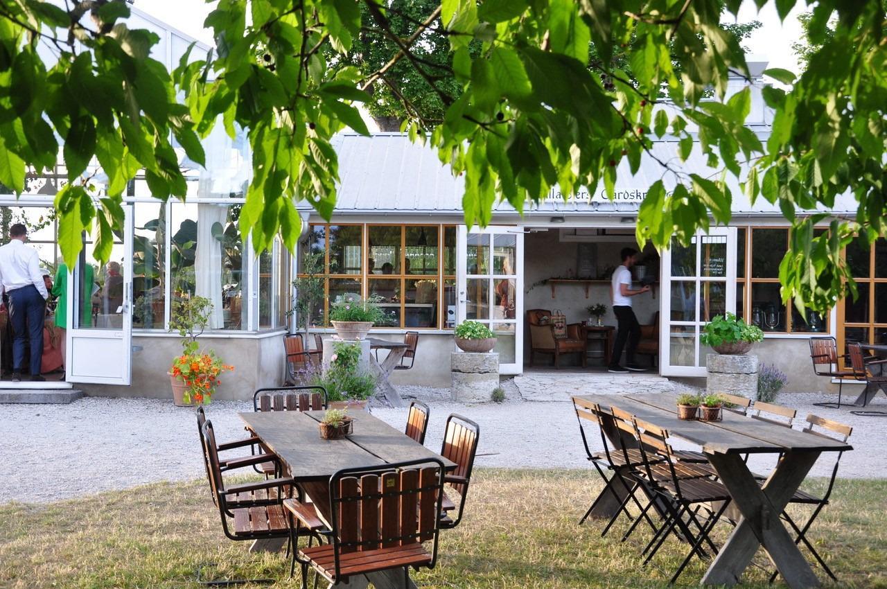 A restaurant set in a greenhouse. Outside the greenhouse is two wooden tables with chairs.