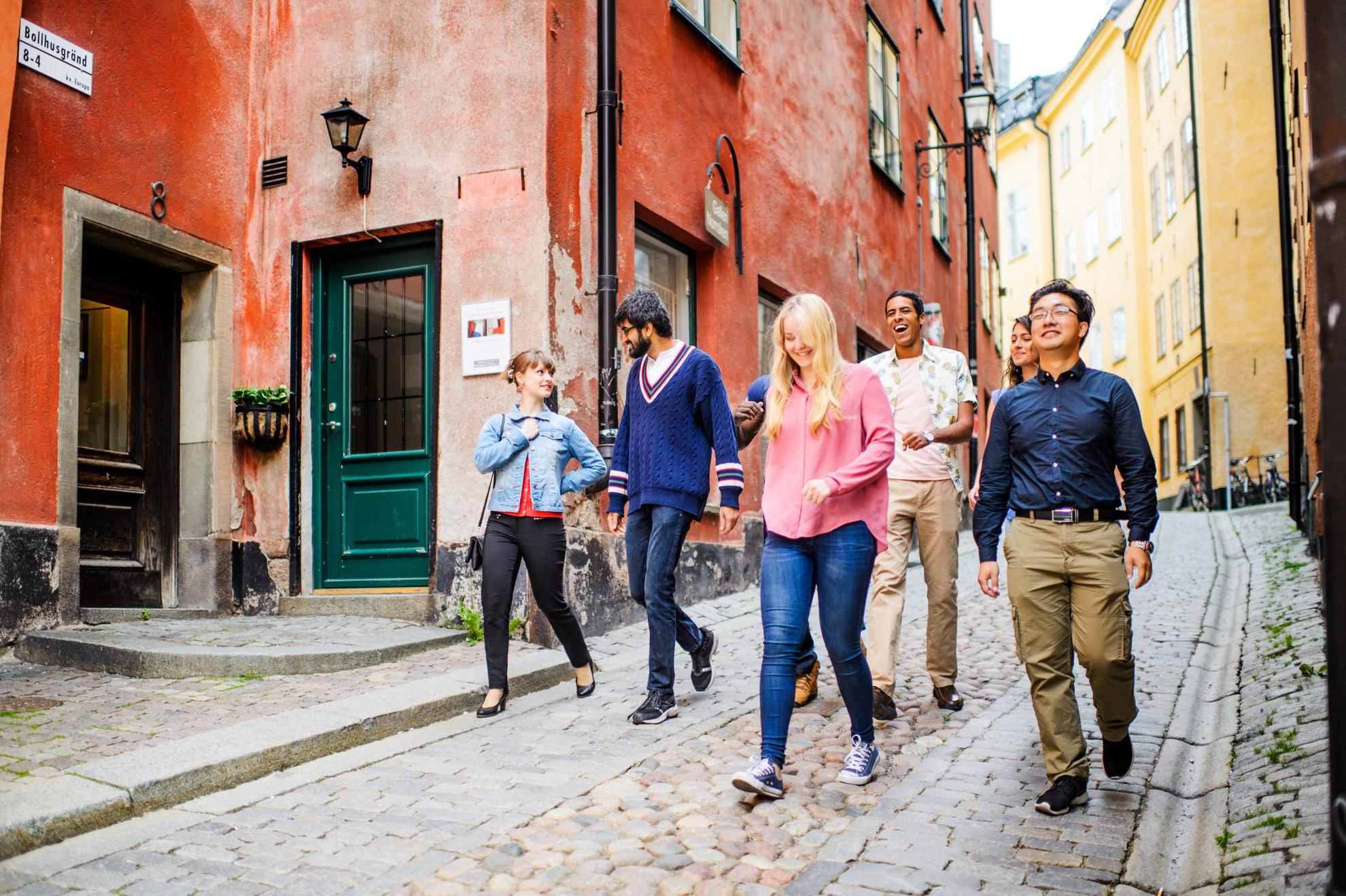 A group of people are walking down a cobbled street in Old Town Stockholm, talking and smiling.