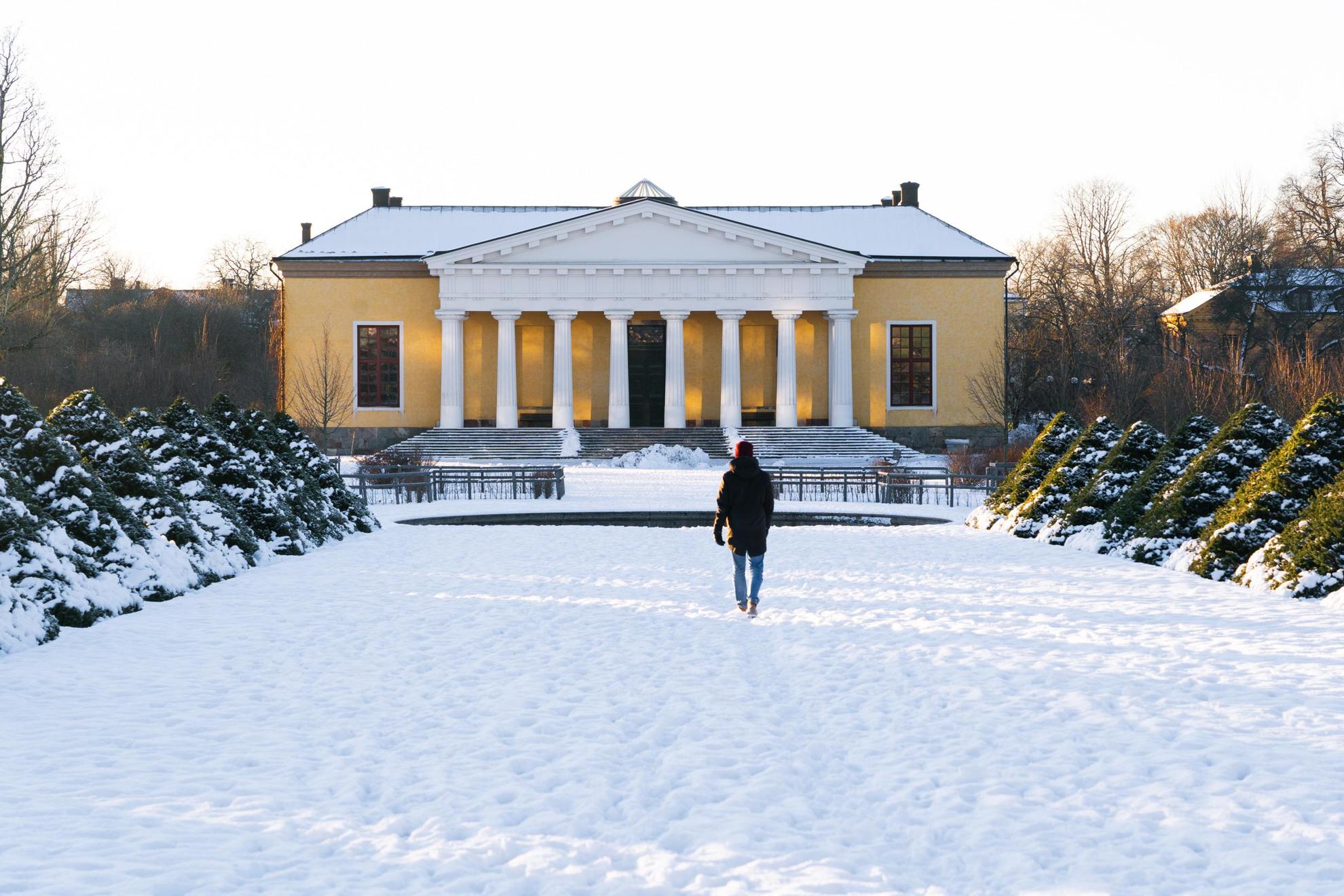 A person walking towards a yellow house at the Uppsala University's botanical garden during the winter.