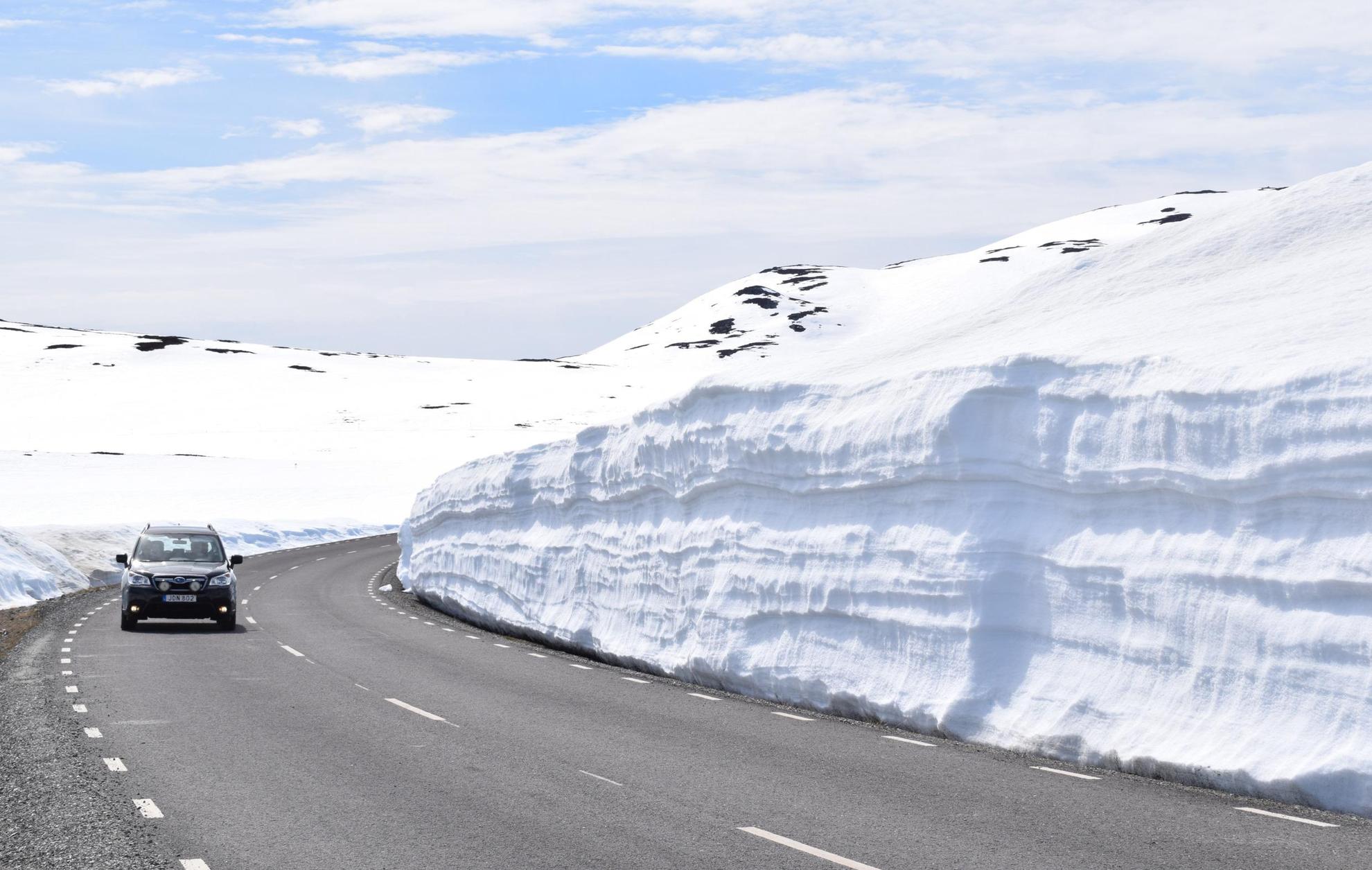 A car is driving on a road surrounded by high snow banks.