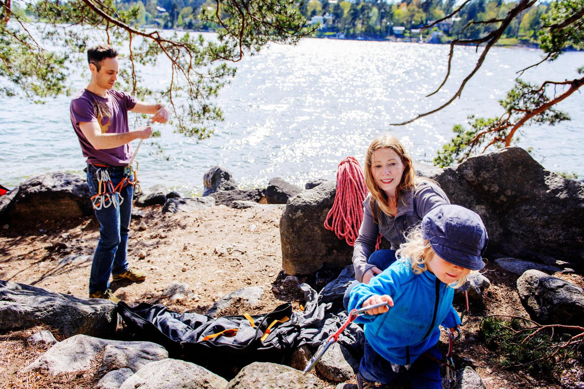 A family by a lake in Bohuslän. The man is preparing his gear. A woman watches a child run away with carabiners in his or her hand.