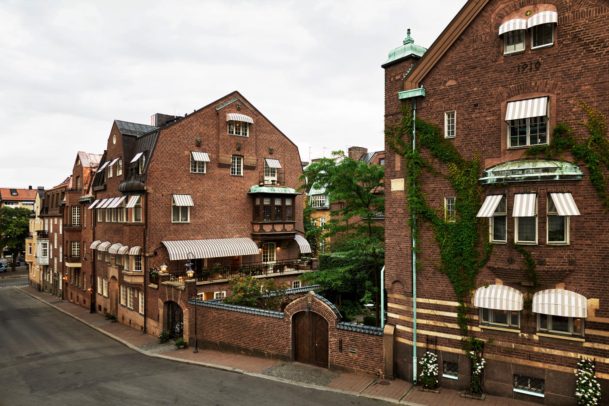 Exterior of an old four story brick house with a garden where you see the top of a flowering bush.