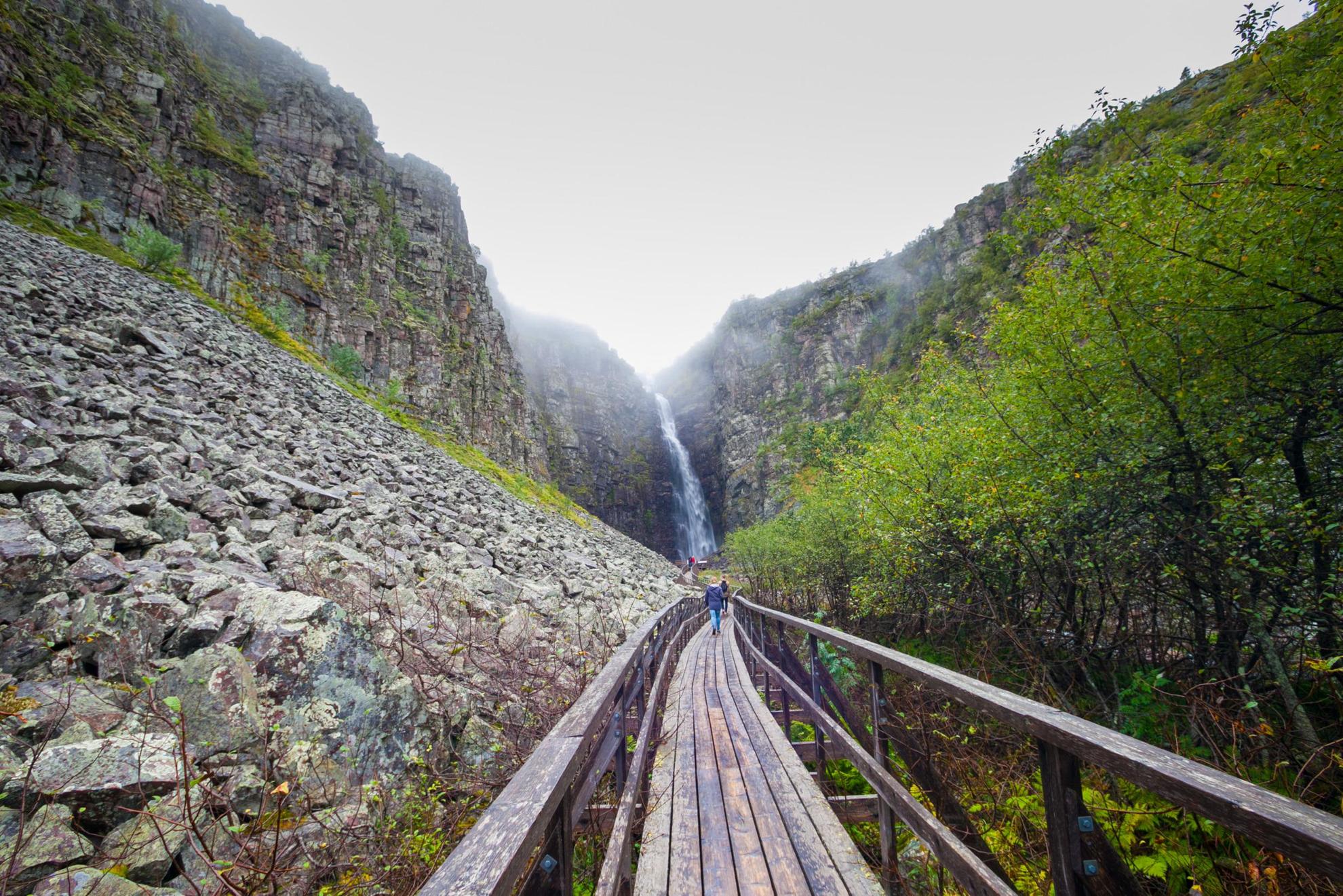 People are hiking on a boardwalk at Fulufjällets National Park, with views of a waterfall.
