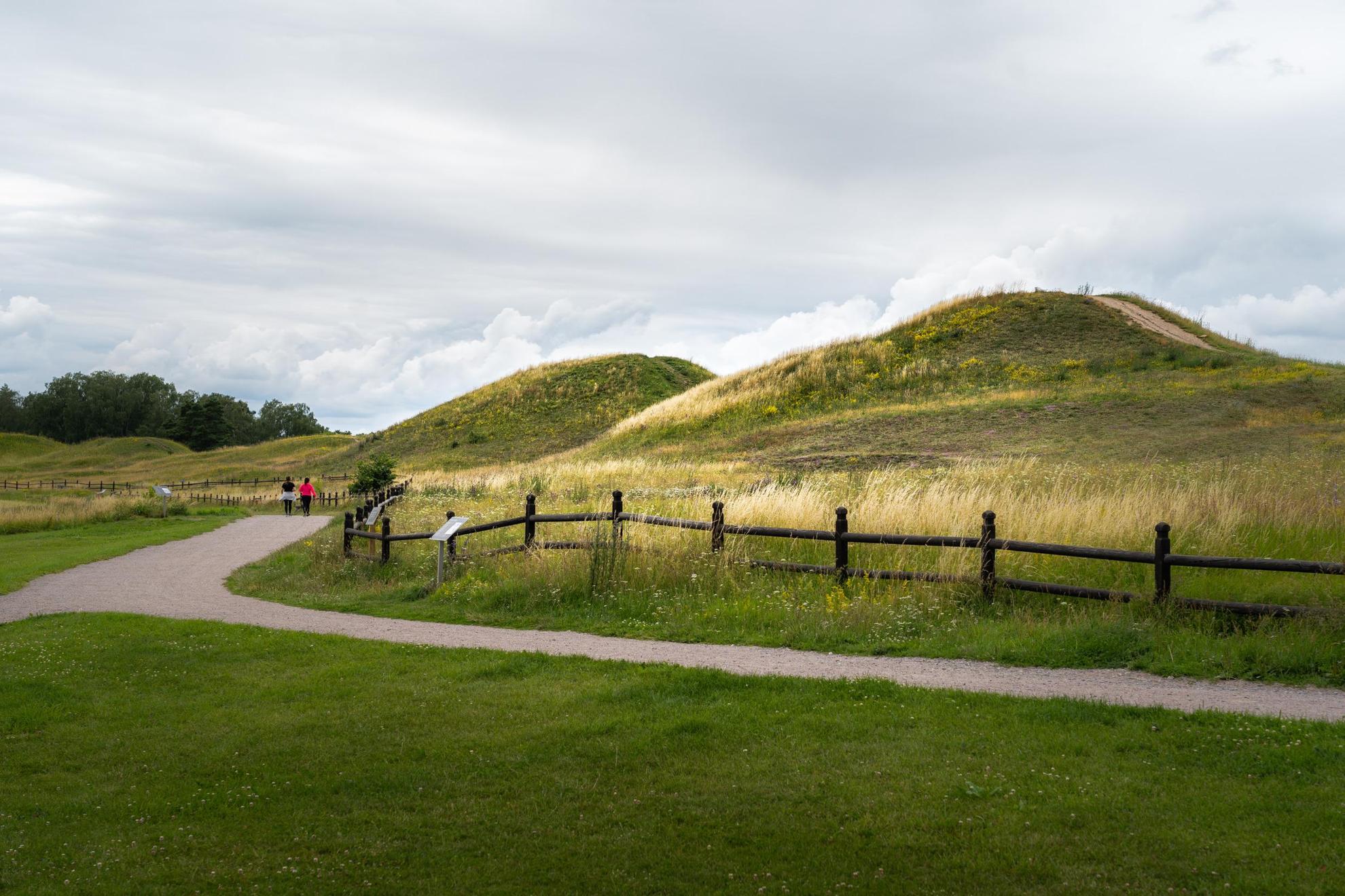 A gravel walkway is next to large mounds covered in grass.
