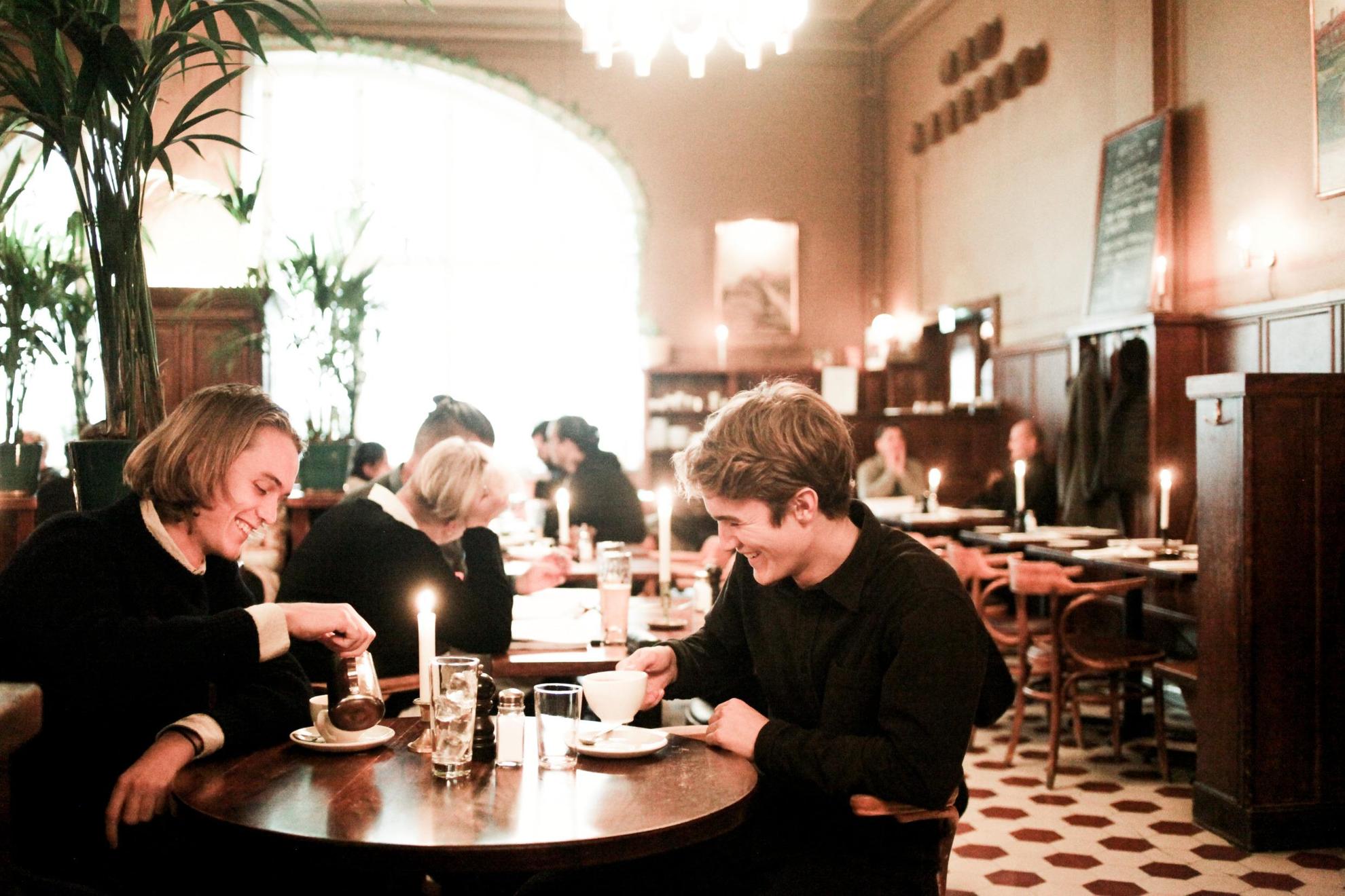 A restaurant setting in Stockholm, where two people in the foreground are enjoying their after-dinner coffee.