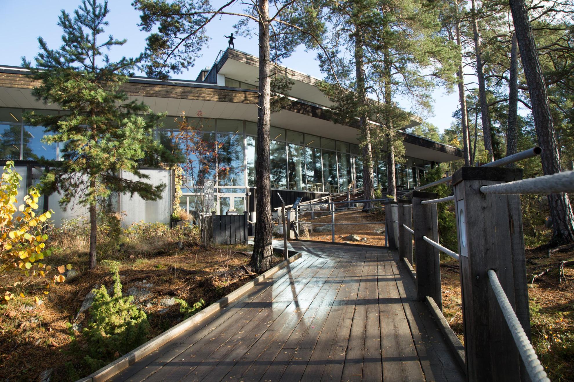 A wooden walkway in the nature that leads up to a house with window walls.
