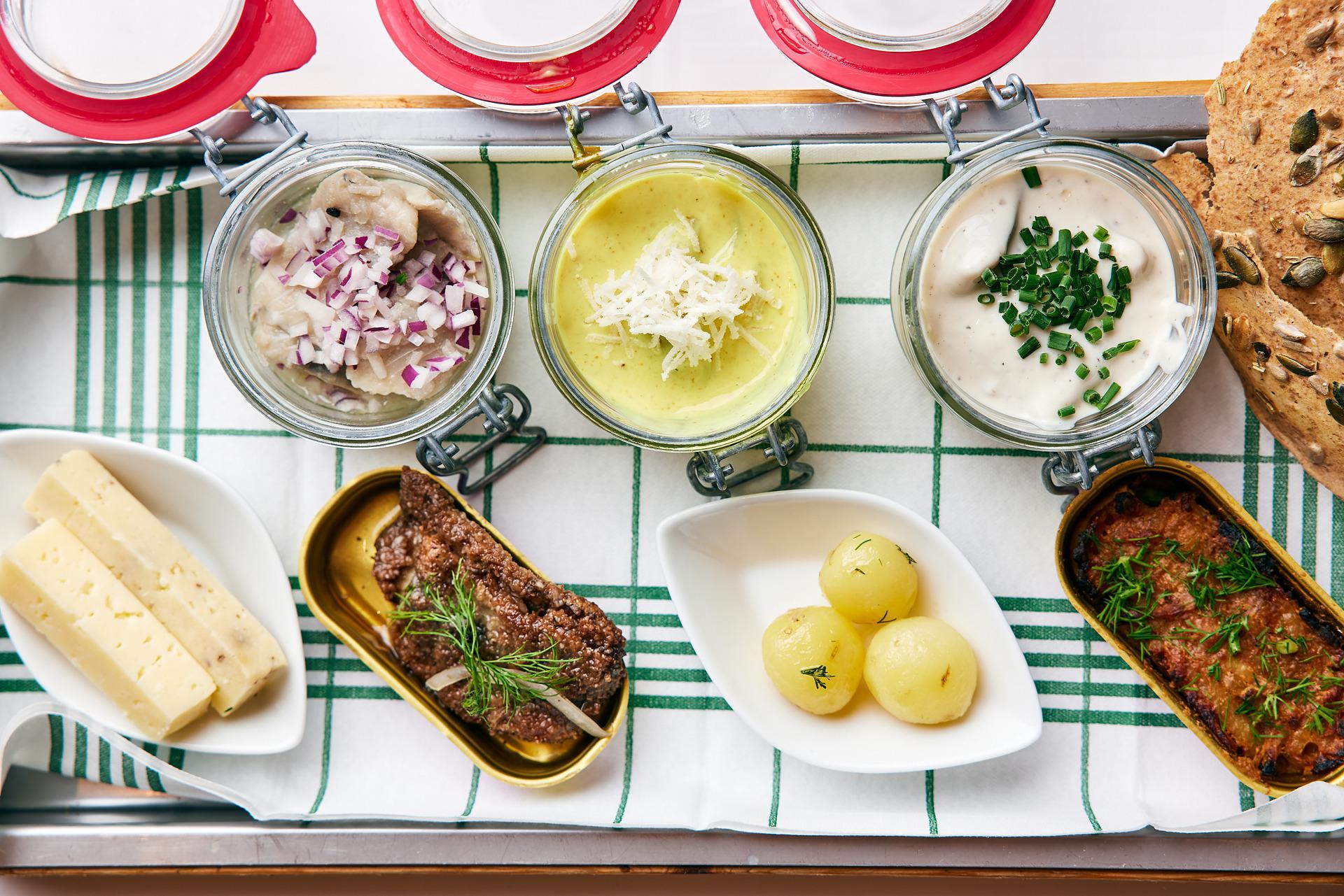 Small bowls of potatoes, herring, meat and cheese, photographed from above.