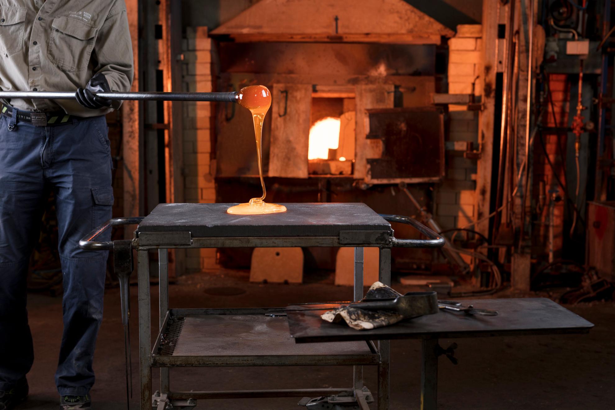A person working with melted glass in front of a furnace.