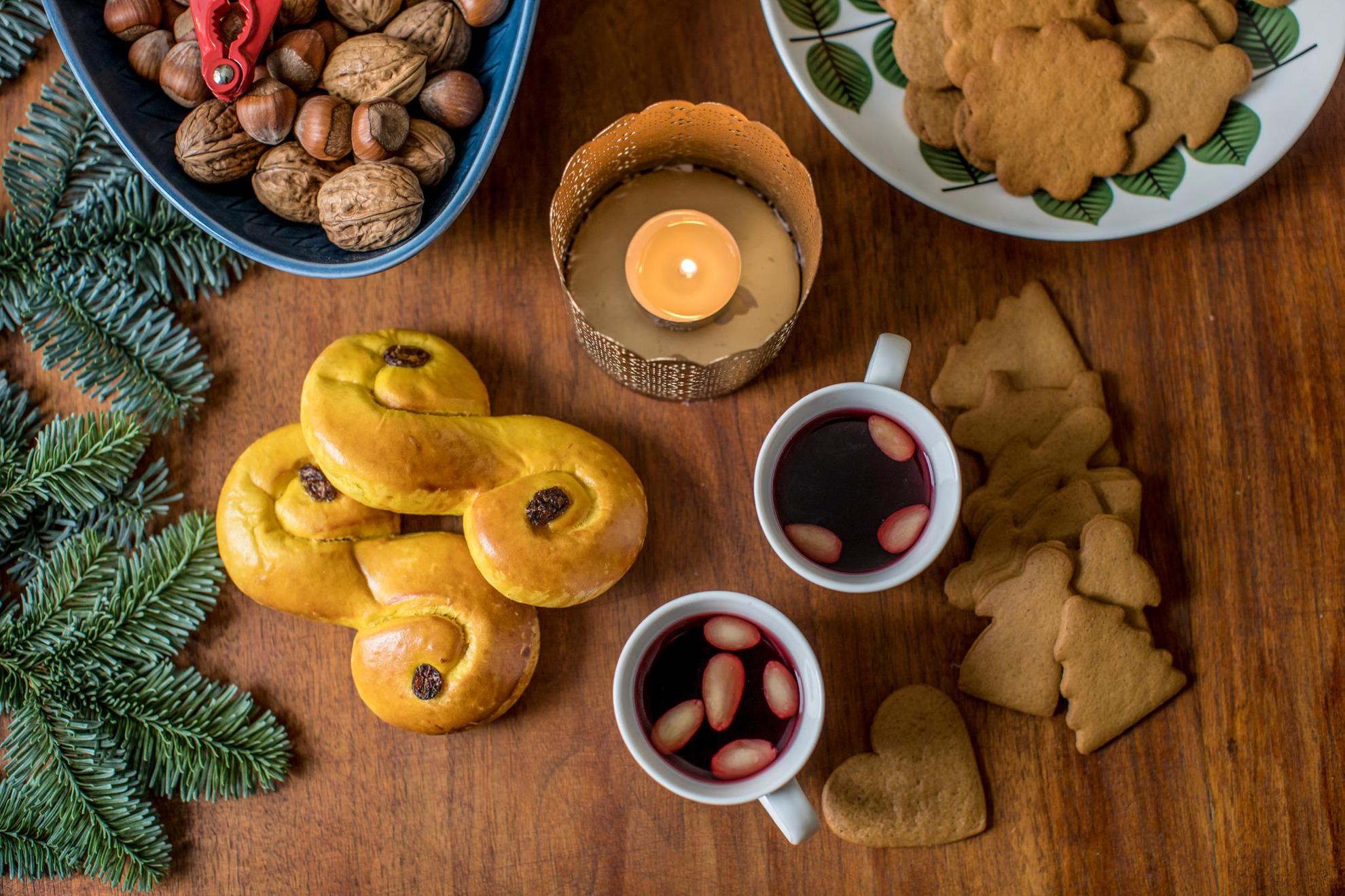 A table spread with typical Swedish Christmas treats and decorations, mulled wine, nuts, gingerbread cookies, lussebullar and pine twigs.