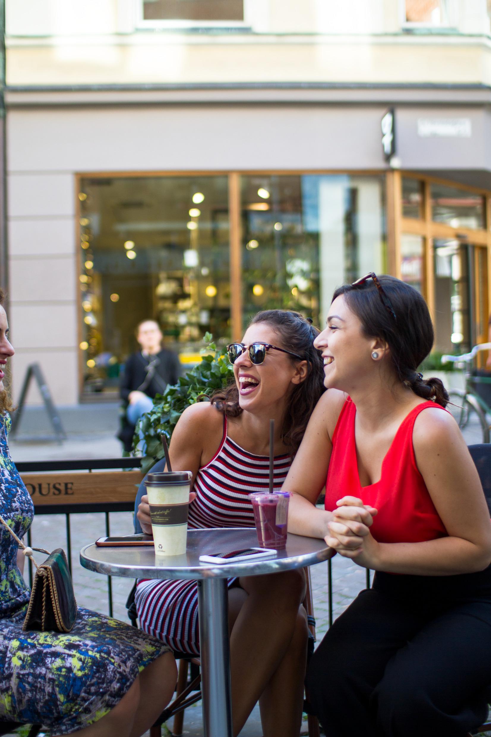 Three women at an outside serving in Malmö having coffee and other drinks and smiling and laughing.