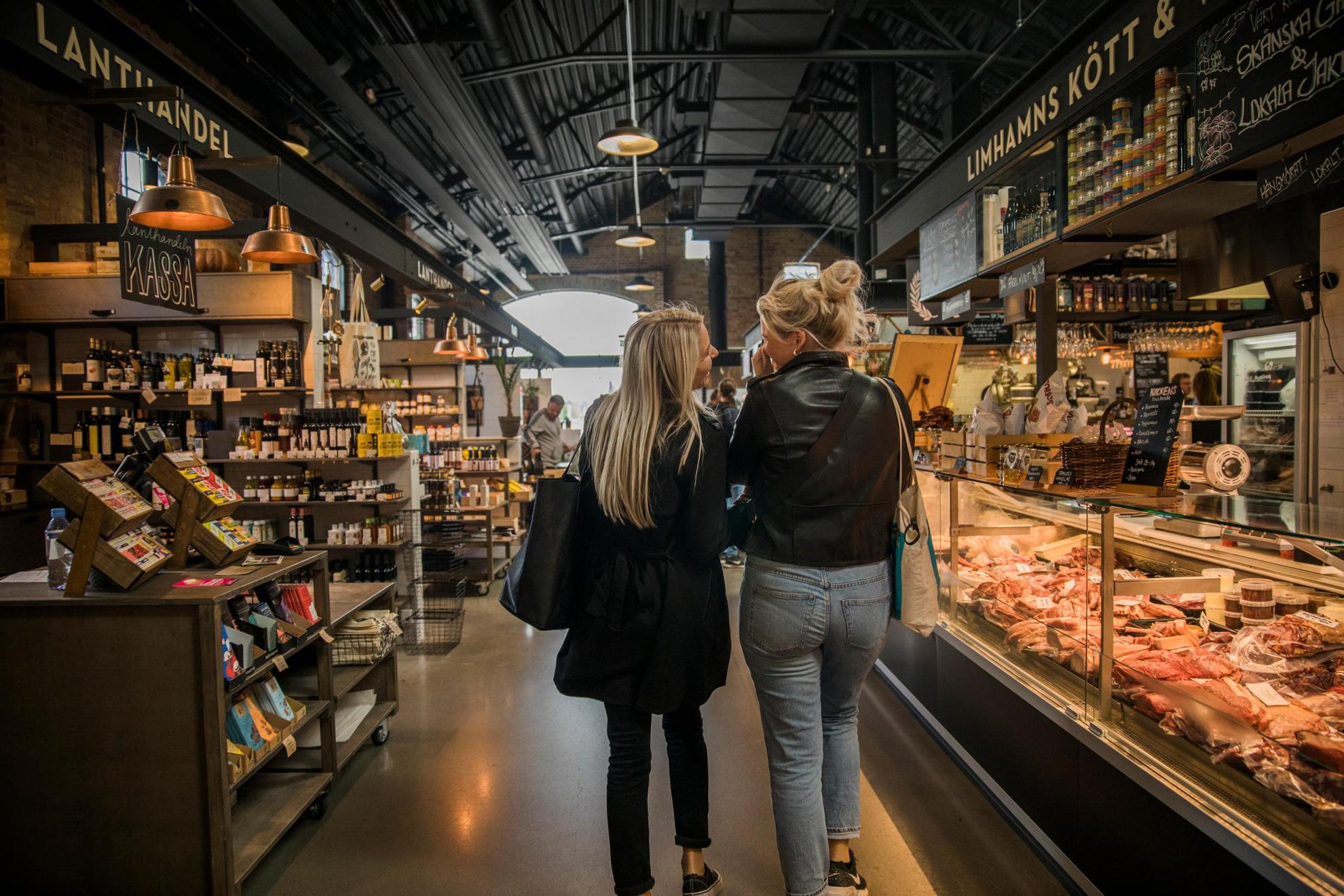 The back of two women that walk and talk in a food market.