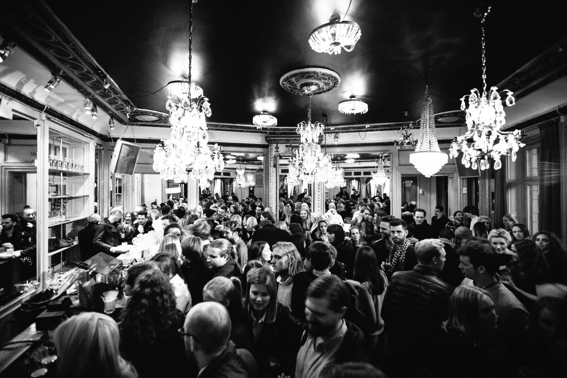 A black and white image of a crowd at Spy Bar in Stockholm. Chandeliers hang from the ceiling.