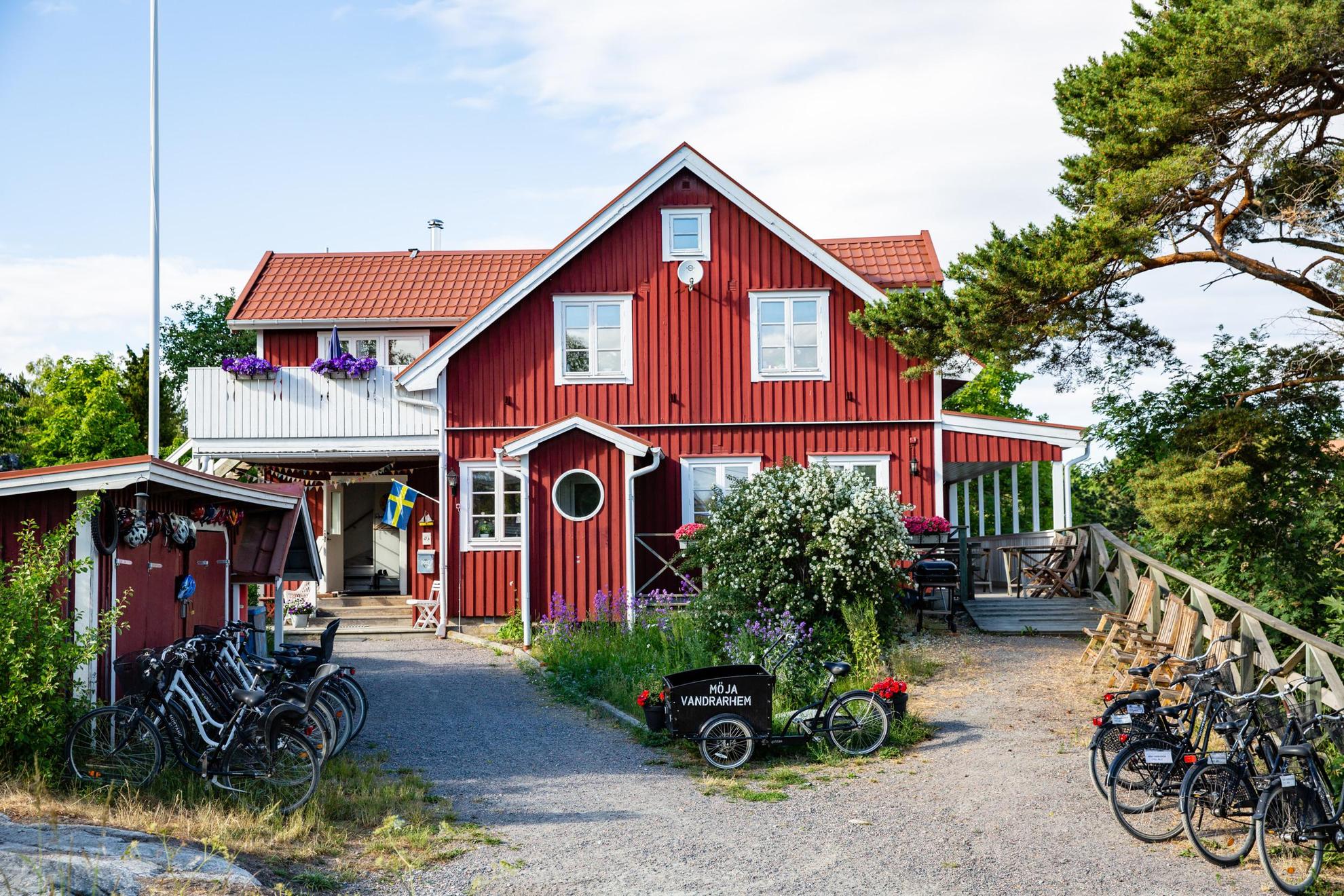 A red wooden house with white trims during summer. Outside the house is several bicycles. On one bike it says "Möja Vandrarhem".