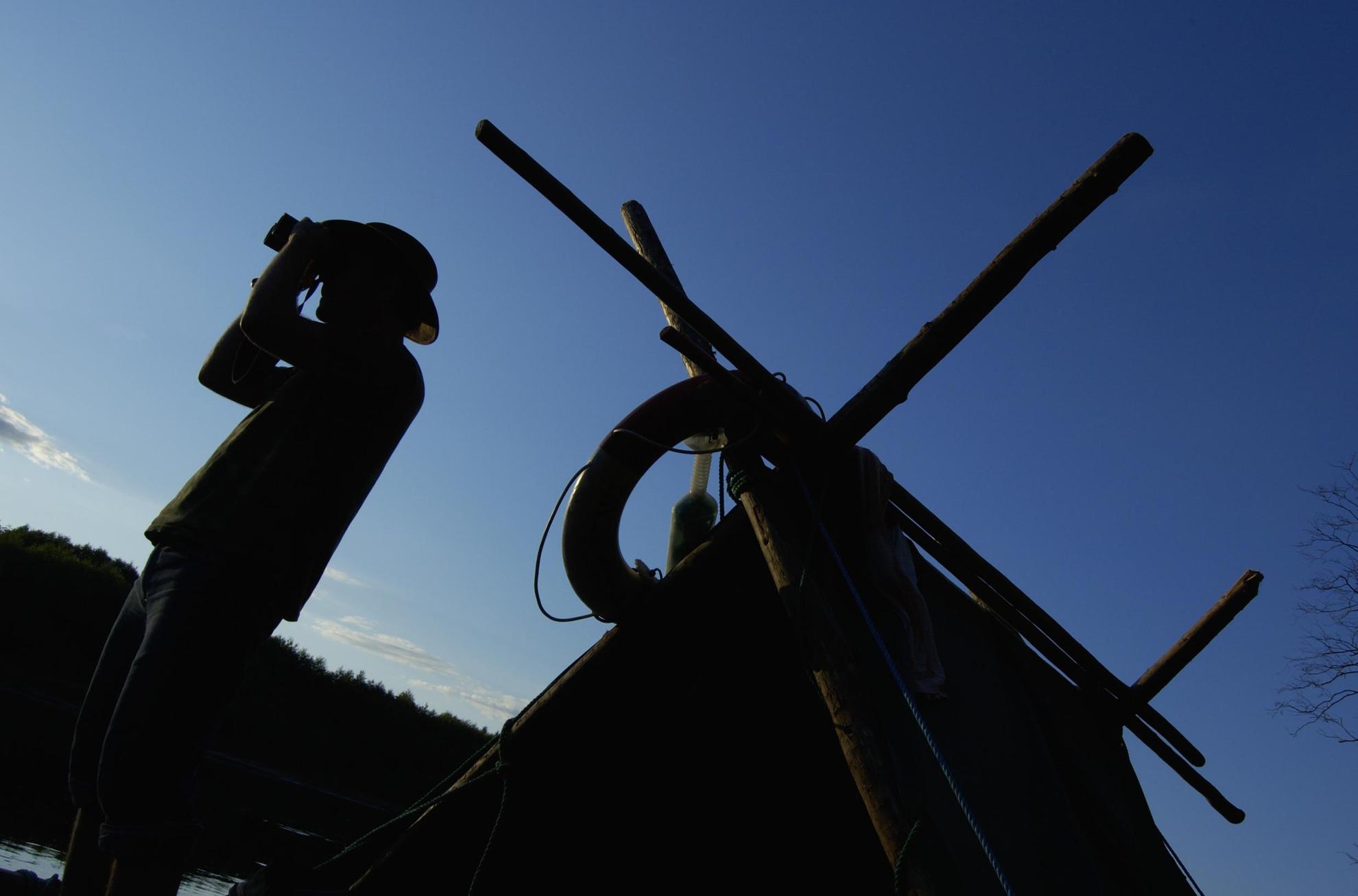 A man on a timber raft in Värmland is looking through his binoculars.