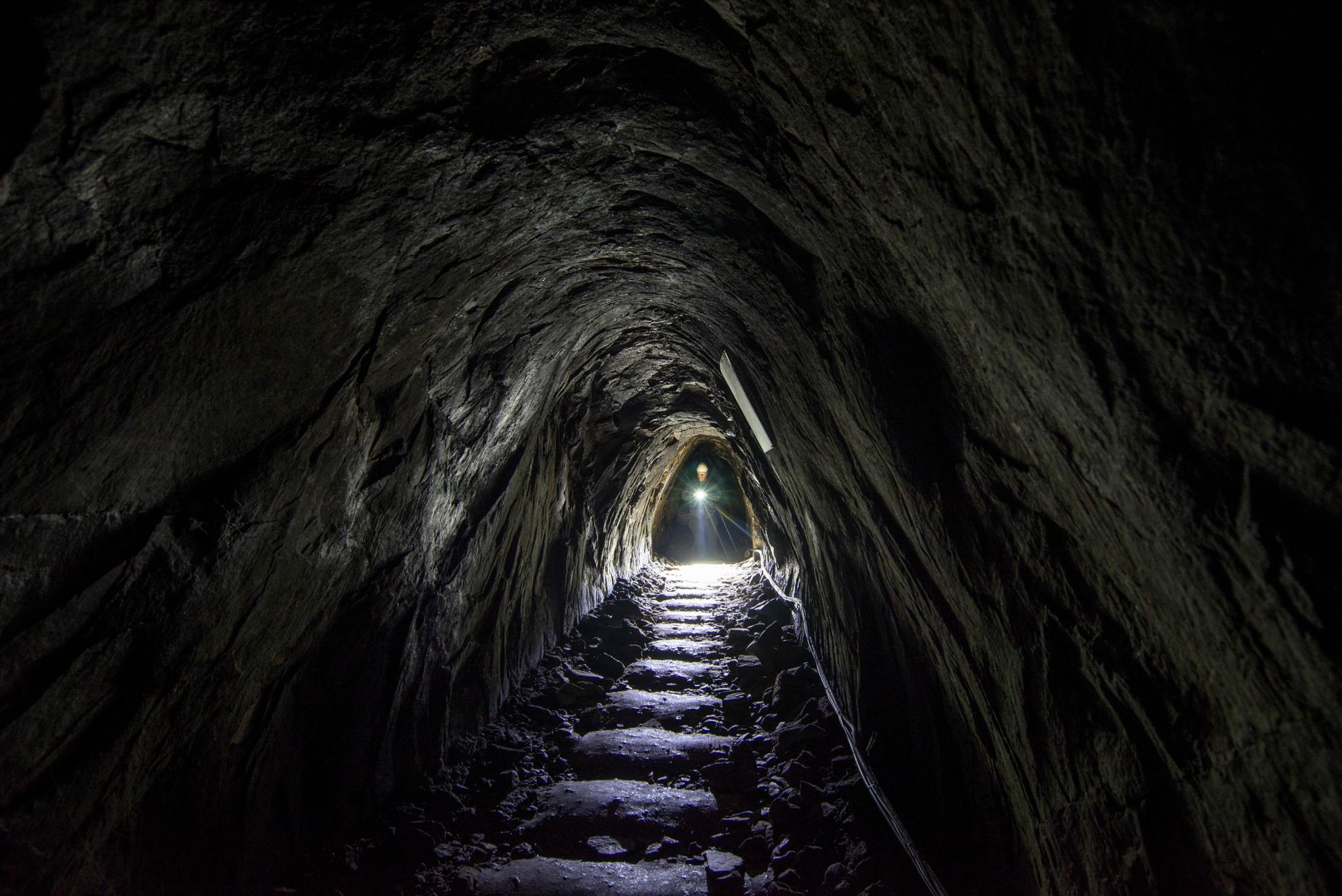 A person with a flashlight walks in an underground passage in Sala Silver Mine.