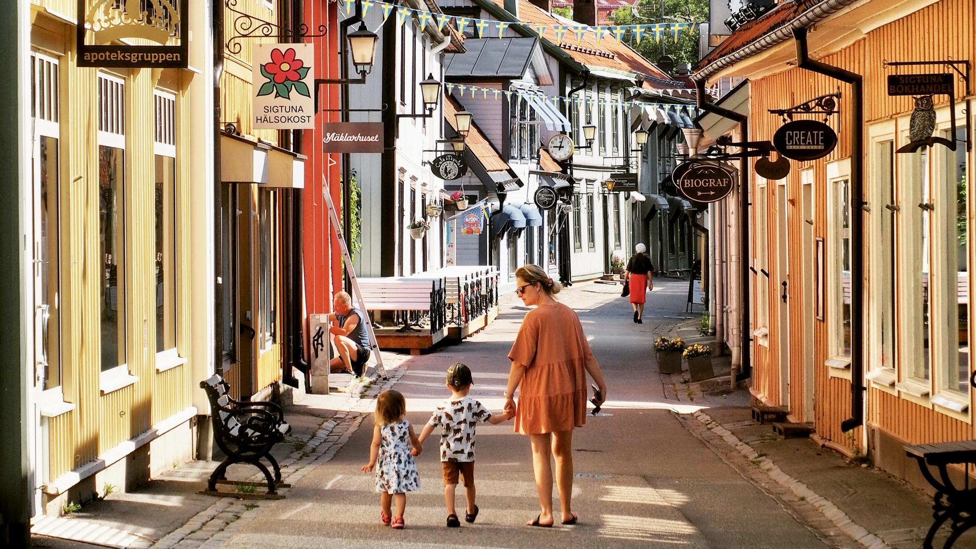Woman in an orange dress with two small children walking through Sigtuna city center on a sunny summer day.