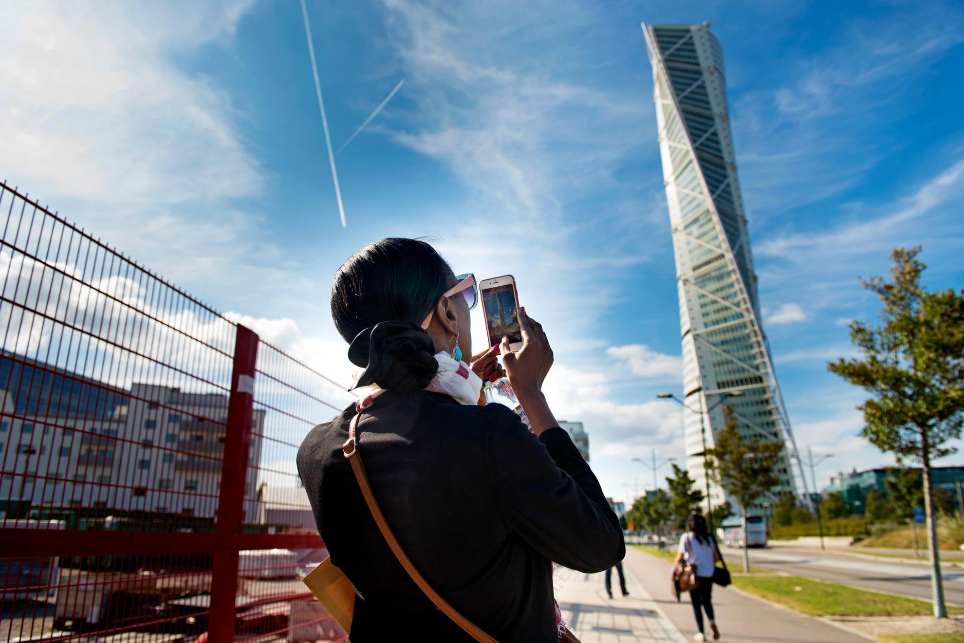A woman is taking a photo of the Turning Torso high-rise in Malmö.