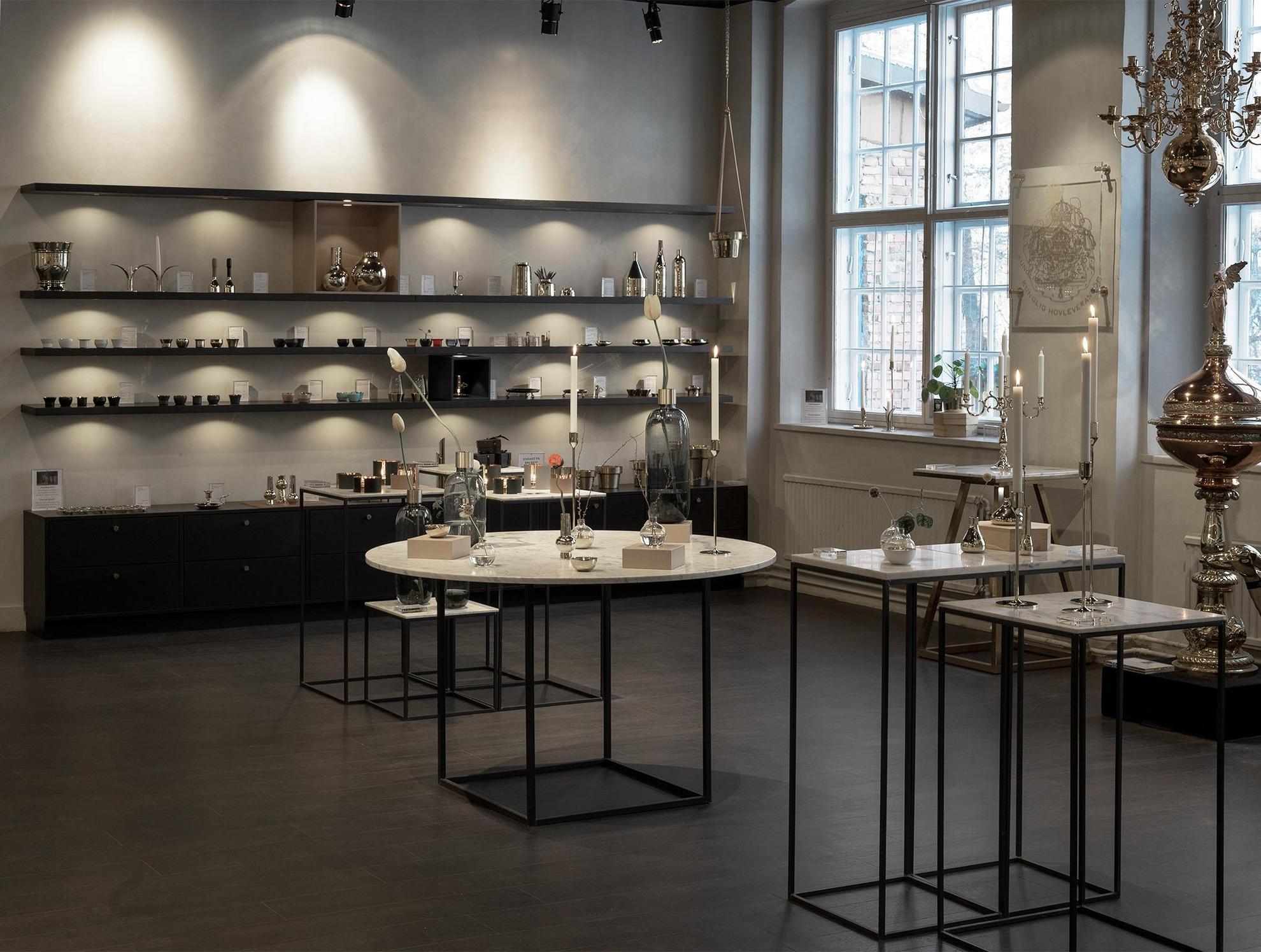 Shop interior of Skultuna Messingsbruk with black shelves and white tables where various products such as vases and candle stick are displayed.