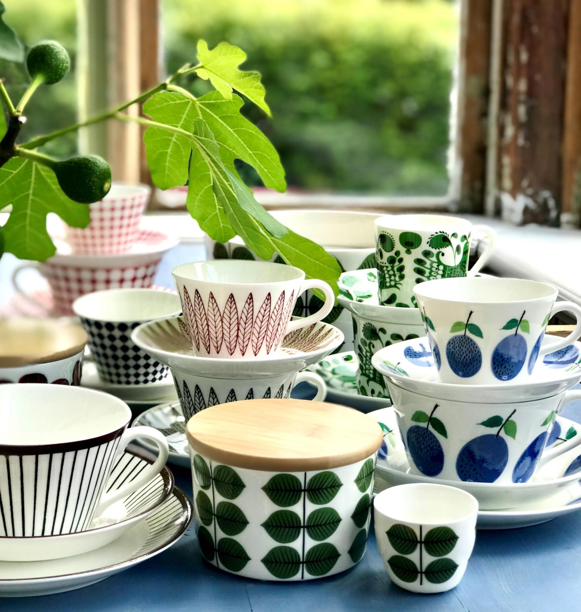 Close-up on porcelain coffee cups with different patterns on a table and a twig from a green plant.