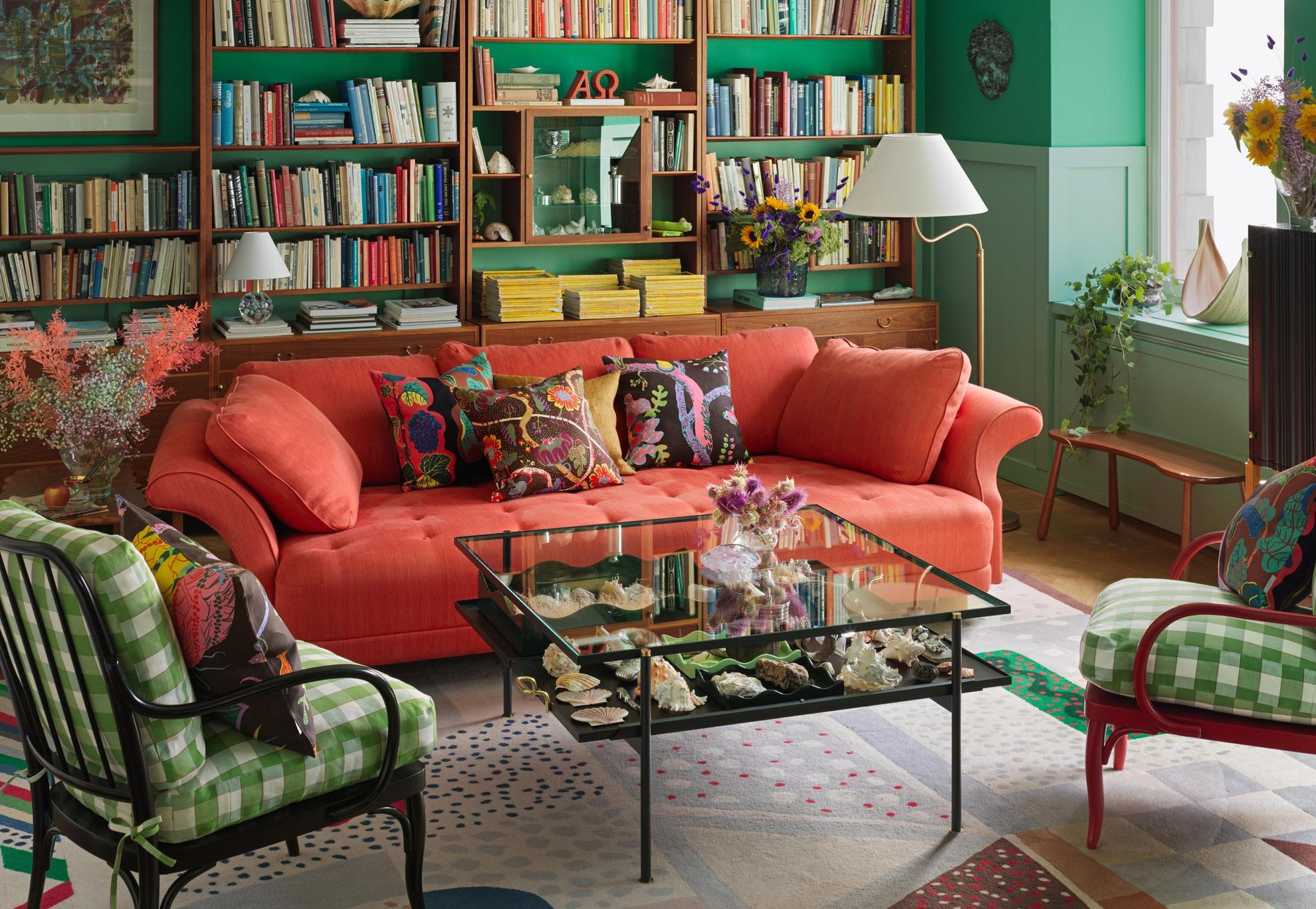 A living room at the interior design store Svenskt Tenn. A square table and two armchairs in front of a red sofa. Vases, books, candlesticks and other interior design items decorates the room.