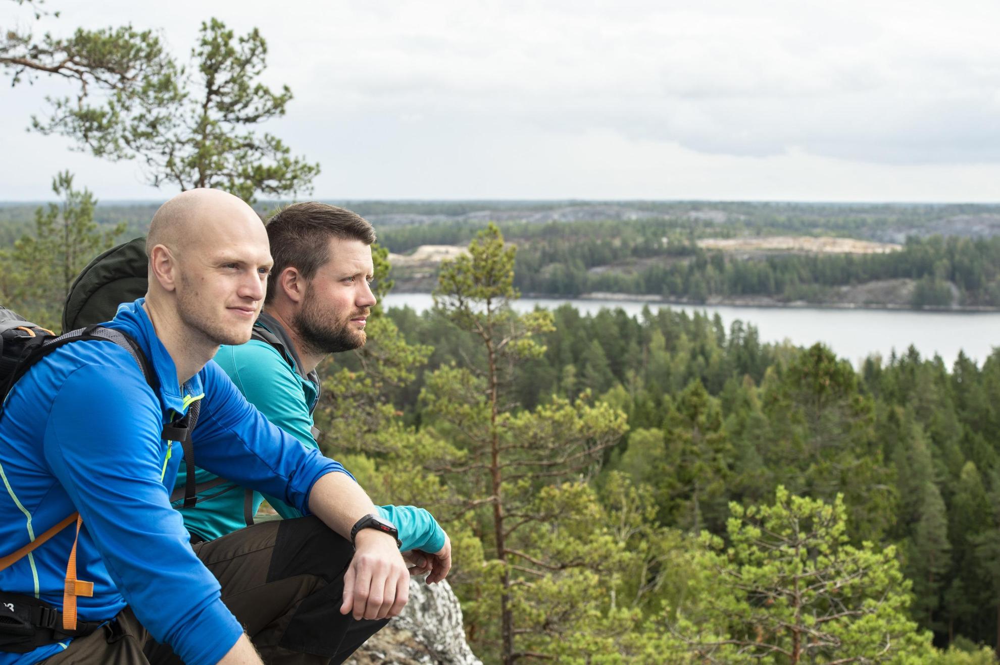 Two men on a hill looking out over forest and a lake.