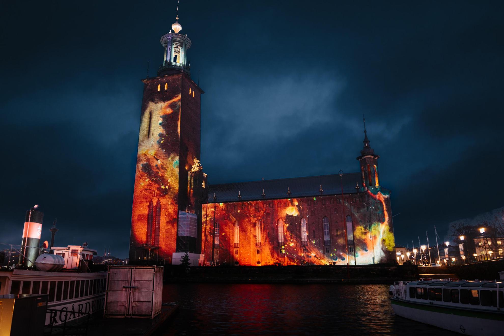 Stockholm City Hall located next to the water is illuminated by a light display during the night.
