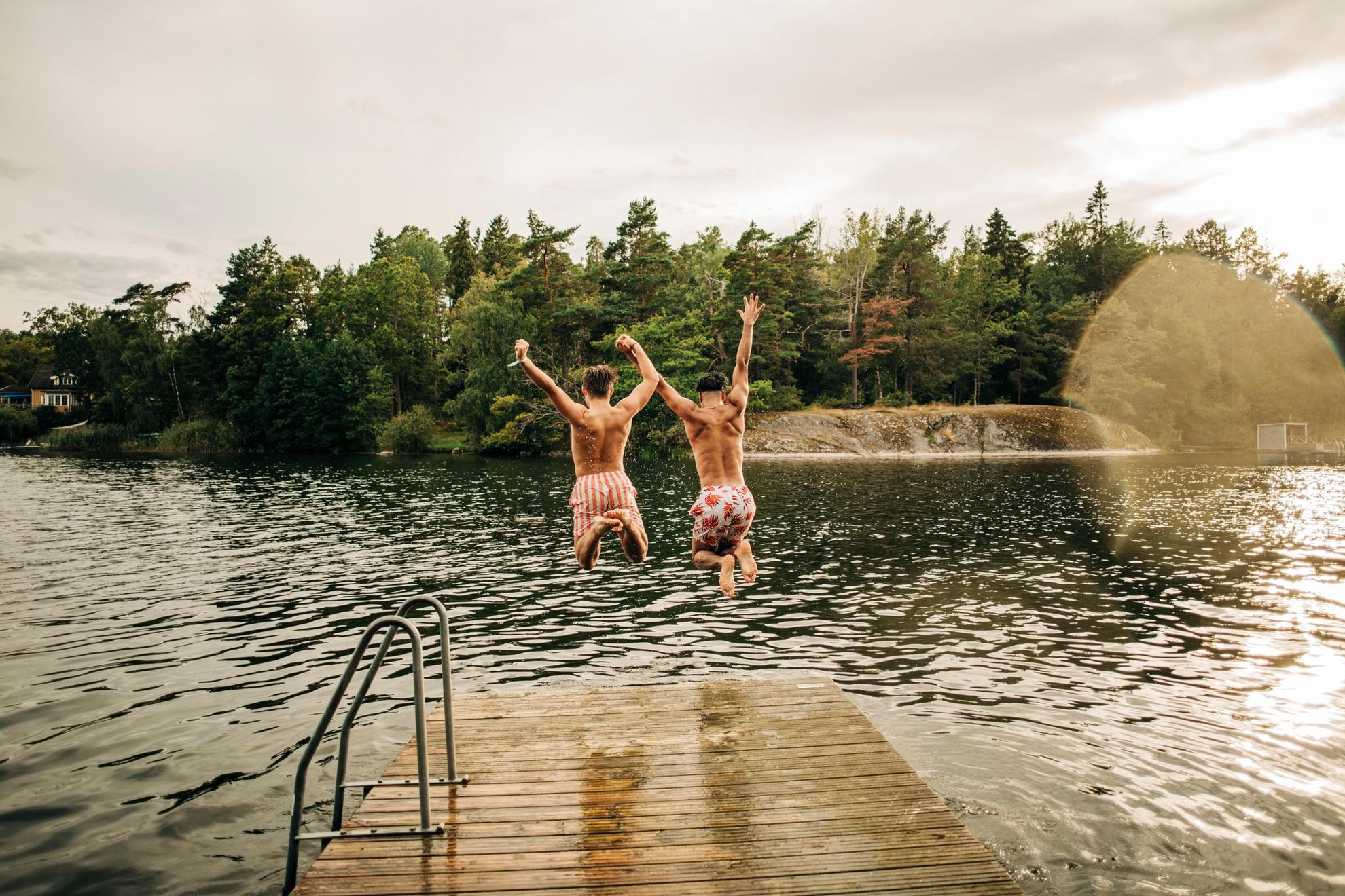 Two men are jumping off a jetty into a lake.