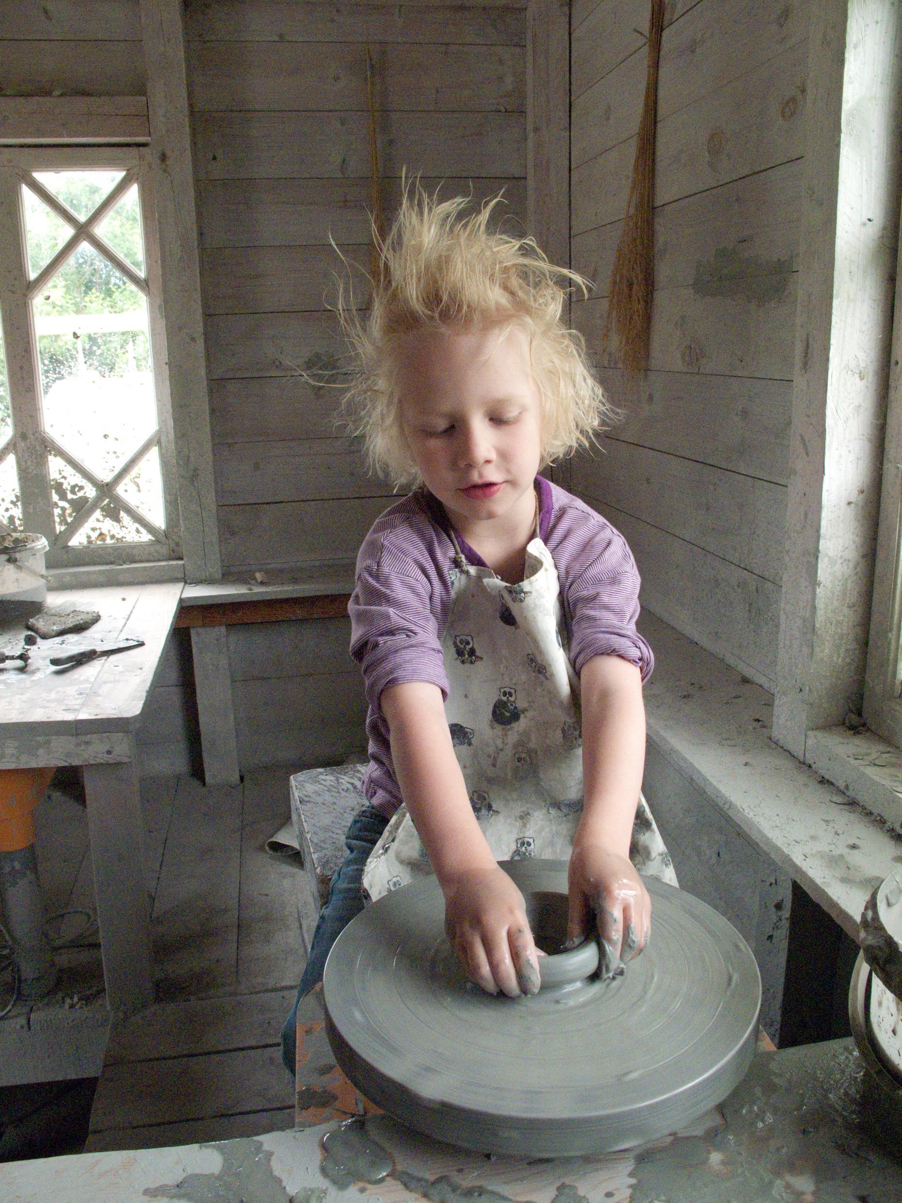 A child wearing an apron is making pottery.