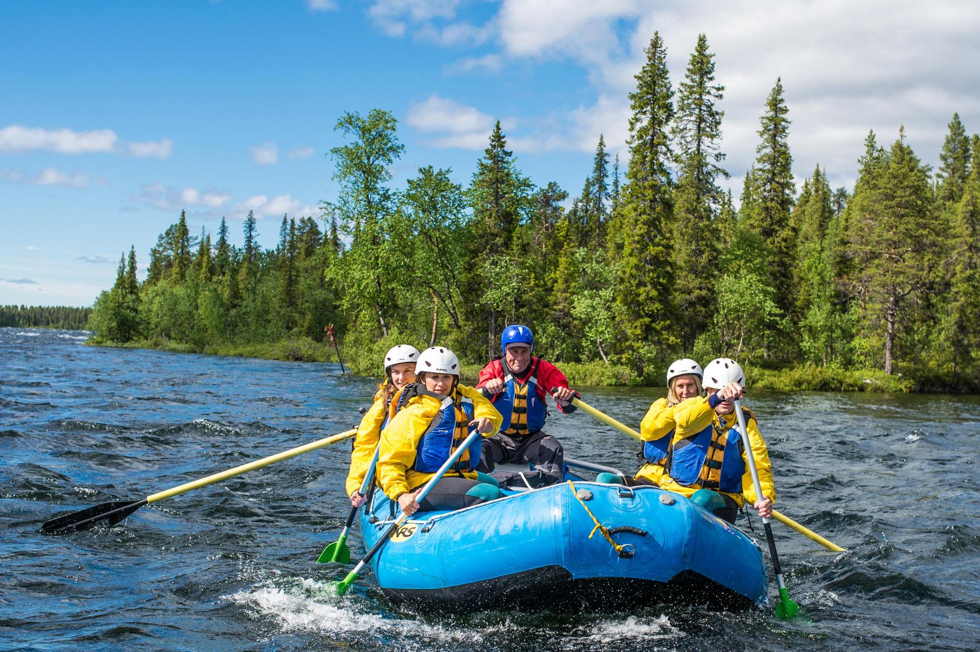A group of five people are river rafting. In the background you see the forest.