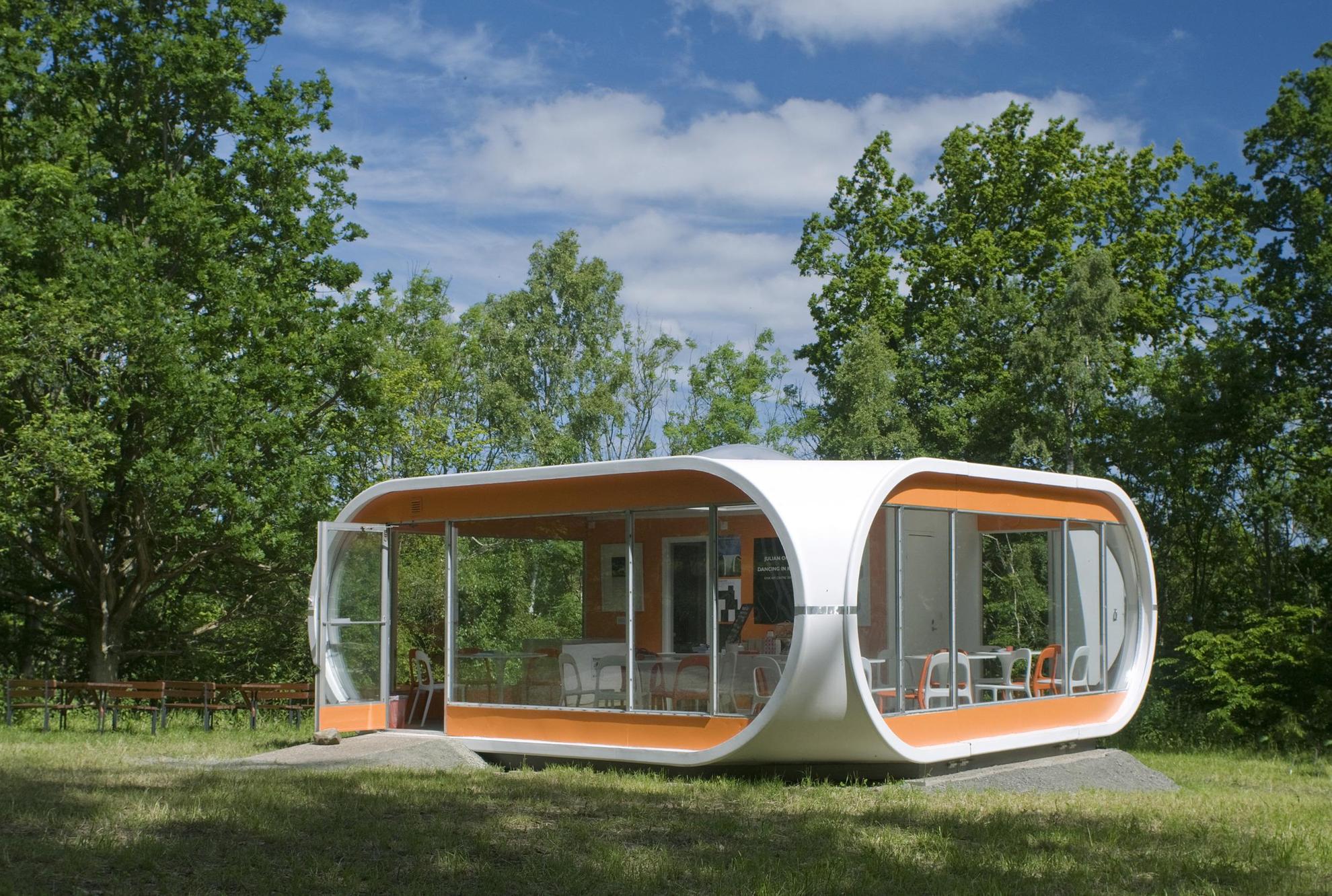 Small cottage made of orange and white plastic set in a green area of Kivik Art Centre.