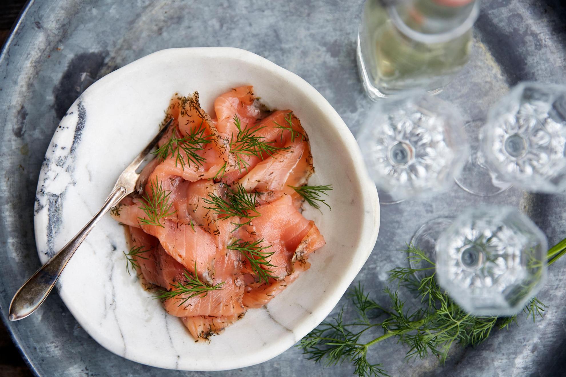 A tray with a plate of cured salmon with dill and a few drink glasses.