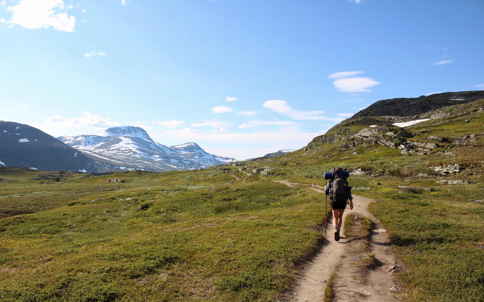 A lone hiker with a large backpack, on a trail surrounded by mountains in Swedish Lapland.