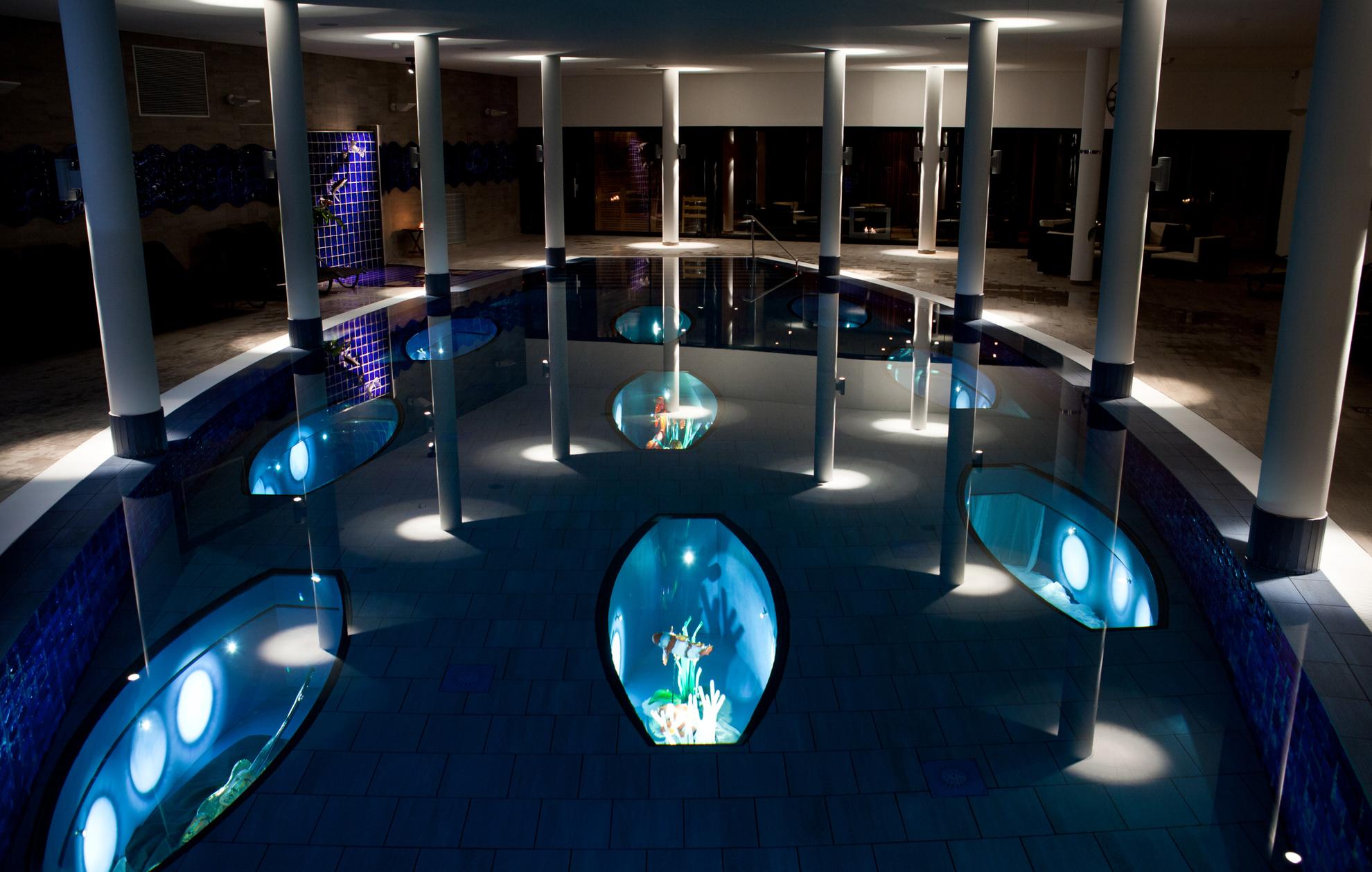 An indoor pool where the light is dimmed. In the pool are illuminated art exhibitions with glass fishes.