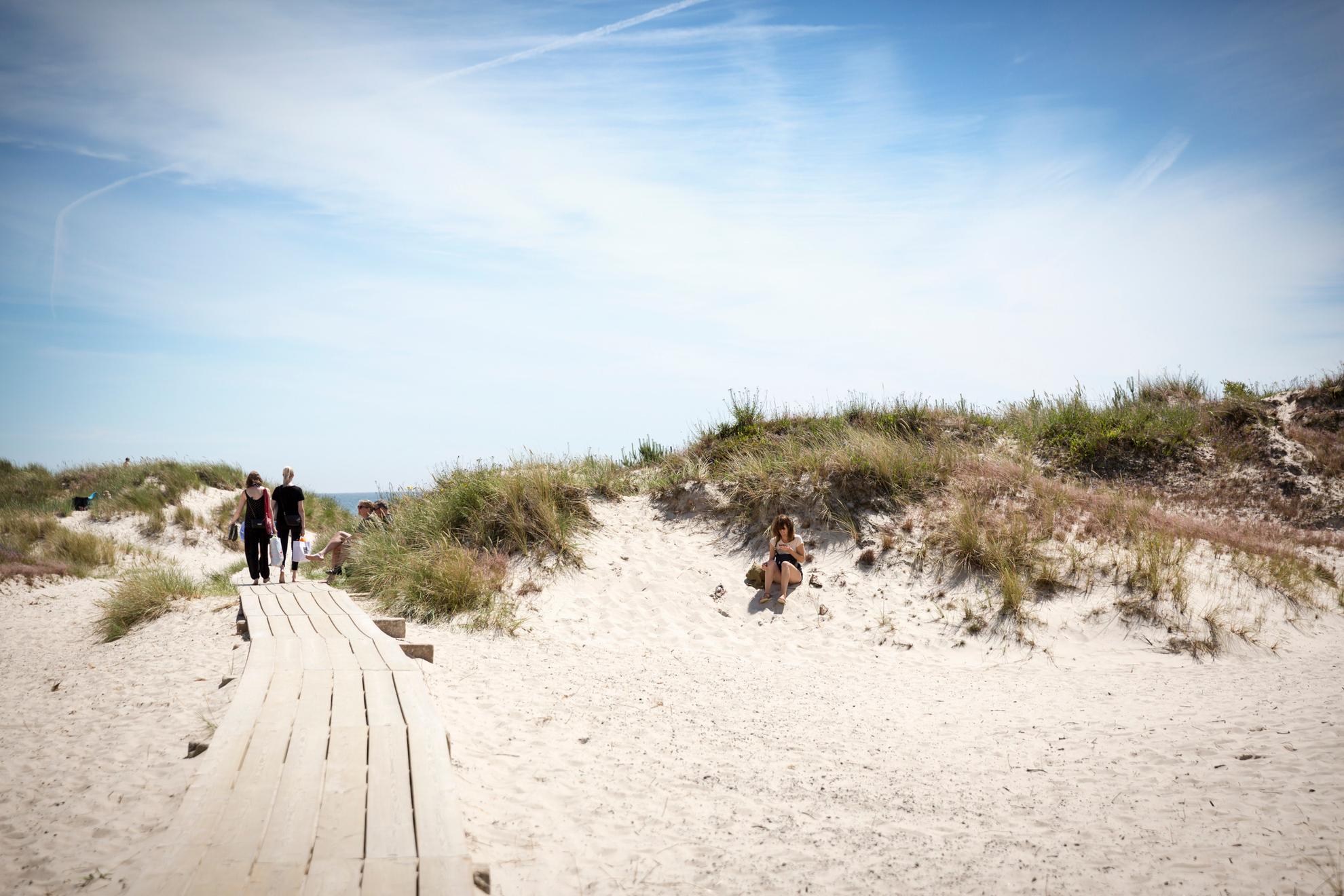 A wooden walkway crosses white sand dunes with tufts of grass.